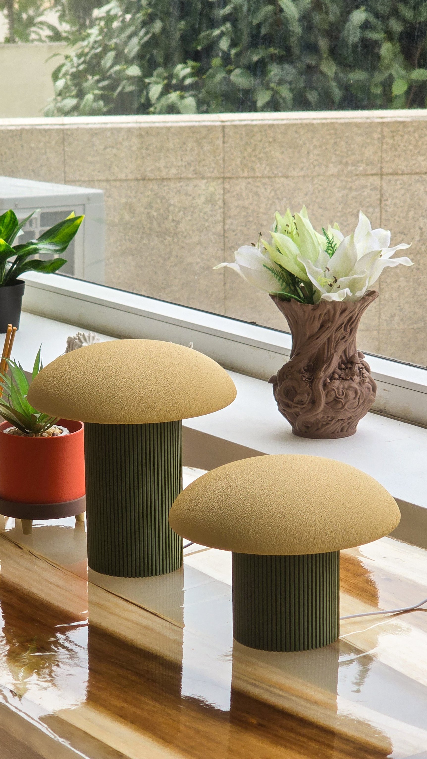 Vasos decorativos com plantas e cadeiras com assentos amarelos posicionados em uma mesa de madeira perto de uma janela com vista para uma parede de tijolos.