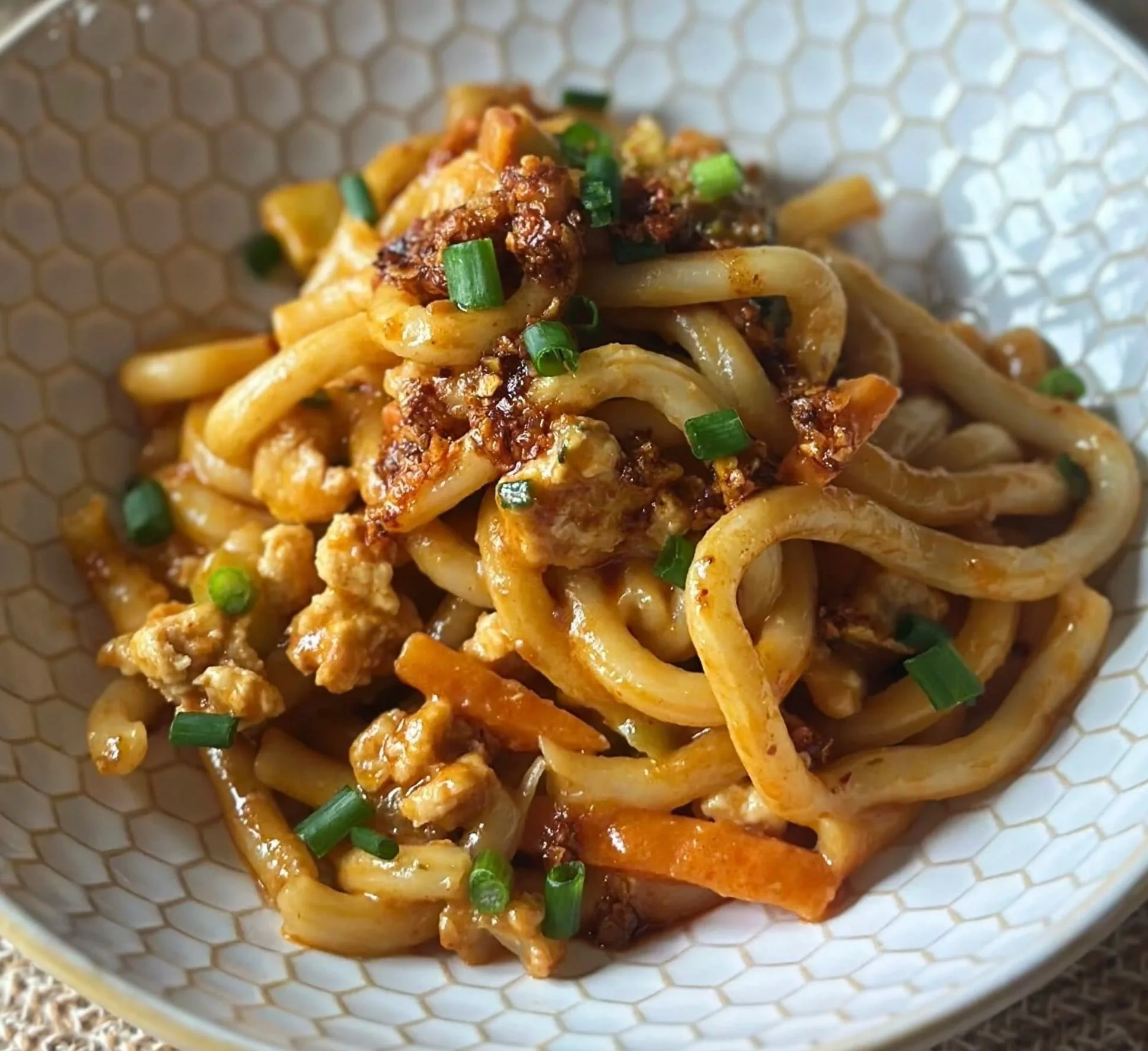 Close-up of a plate of Asian-style stir-fried noodles with ground meat, vegetables, and green onion garnish.