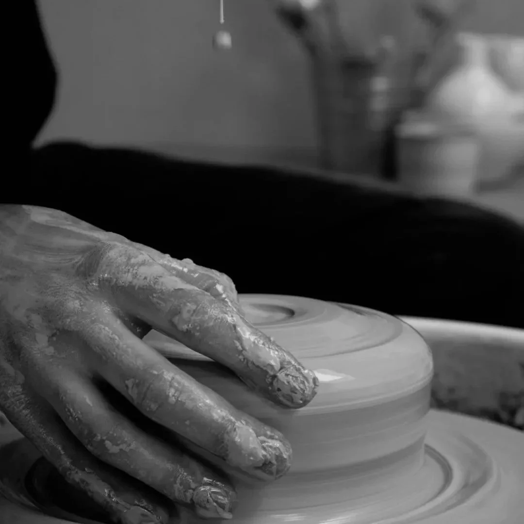 Eine Hand, die Ton auf einer Töpferscheibe formt, in Schwarz-Weiß aufgenommen.