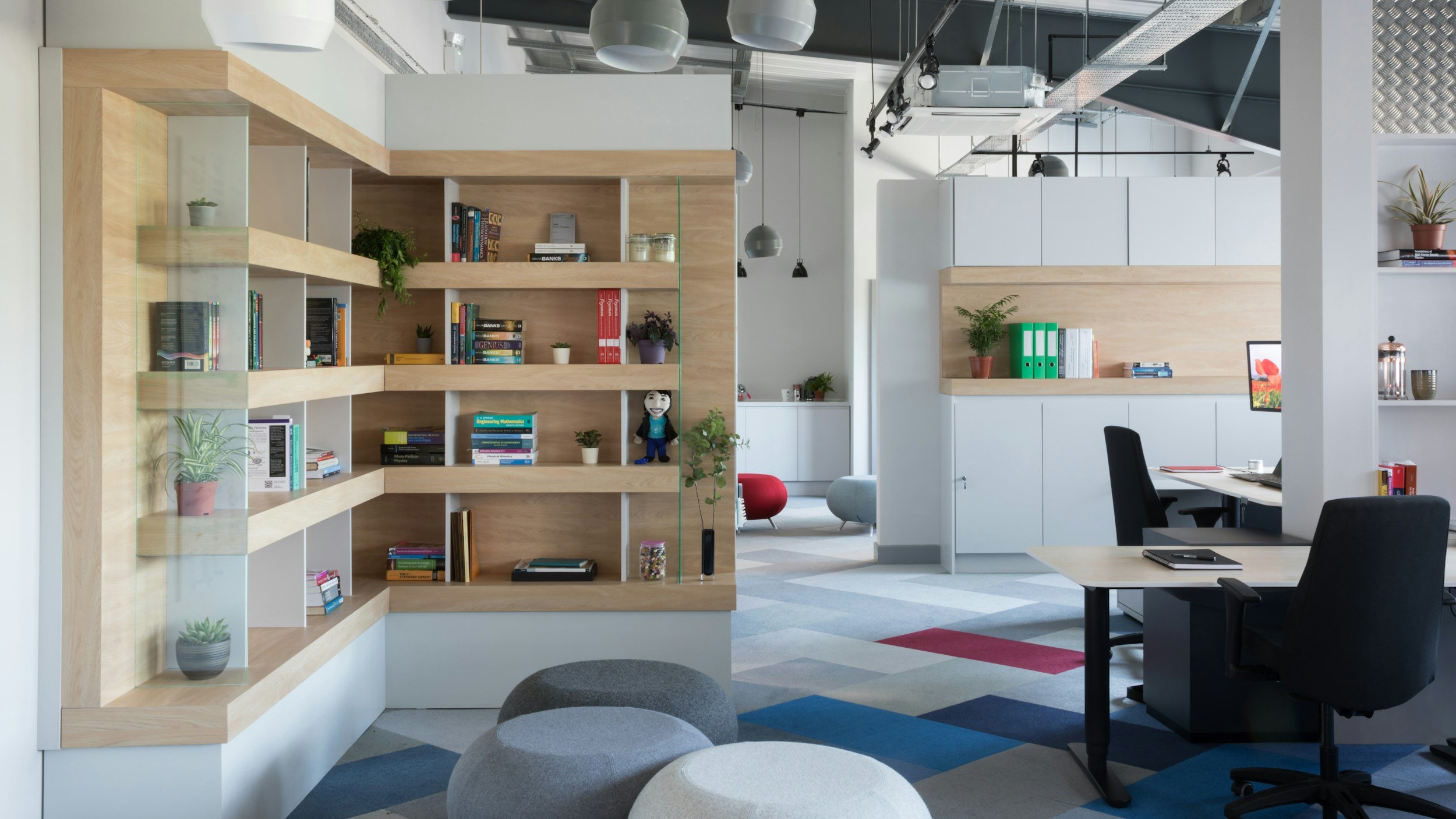 Modern office space with bookshelves, plants, and a workspace with a computer.