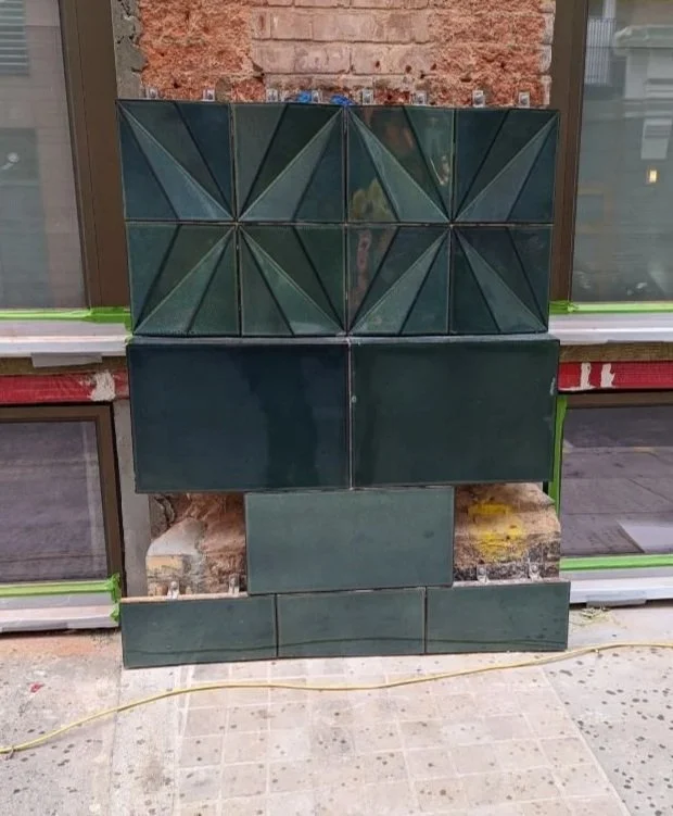 The facette green tiles with geometric patterns mounted on a brick wall.