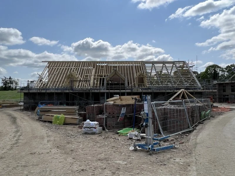 Construction site of a house with a wooden roof frame under a partly cloudy sky.