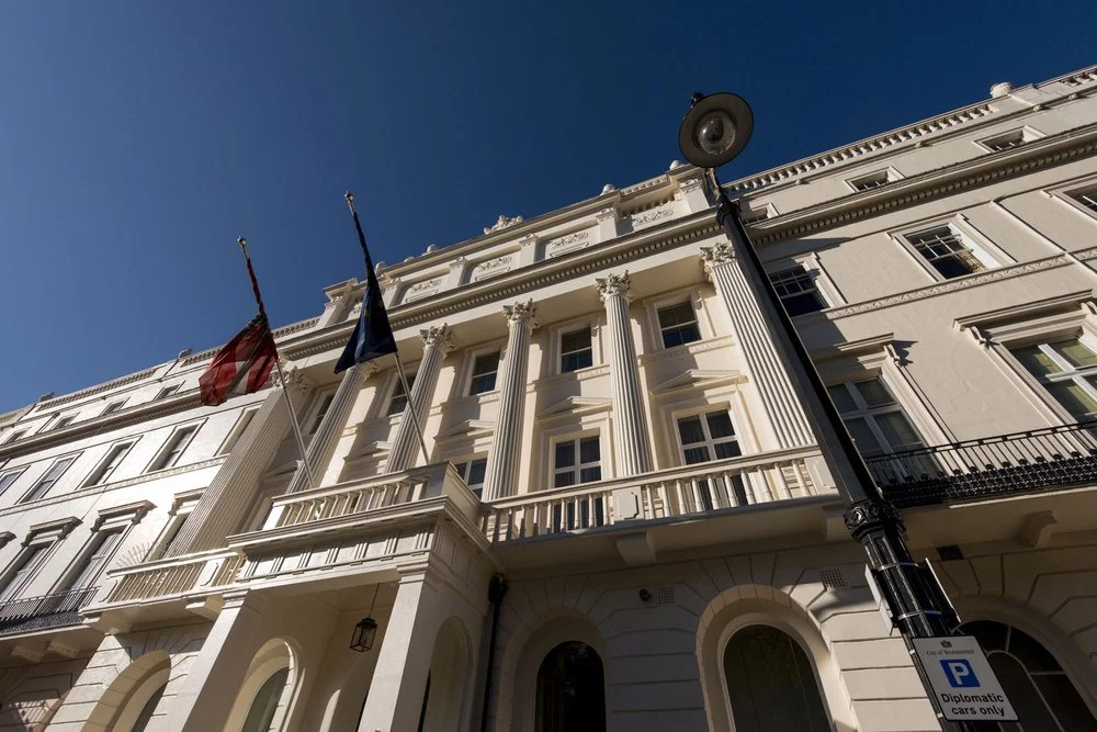 White historic building with tall columns, flags, and a street lamp under a clear blue sky.