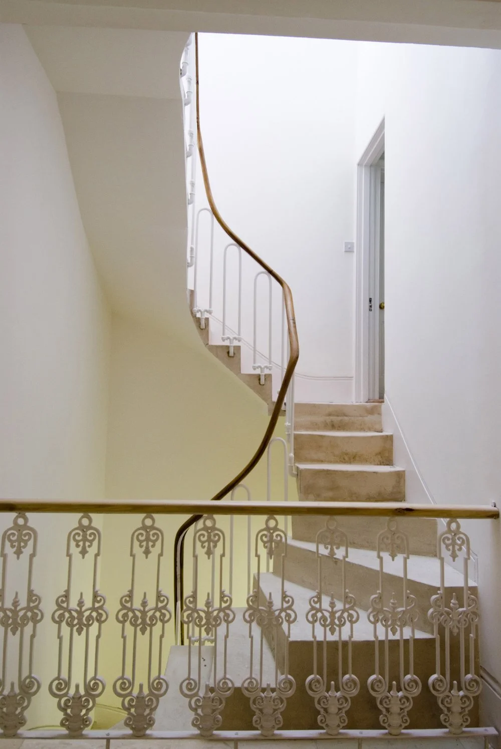 New minimalist helical concrete staircase at the Austrian Cultural Forum, designed and built by NBA, featuring a flowing timber handrail and white curved balustrades.