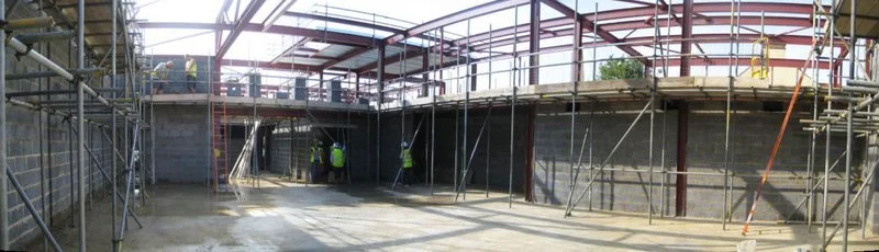 Construction workers on a building site with scaffolding and a partially completed metal roof