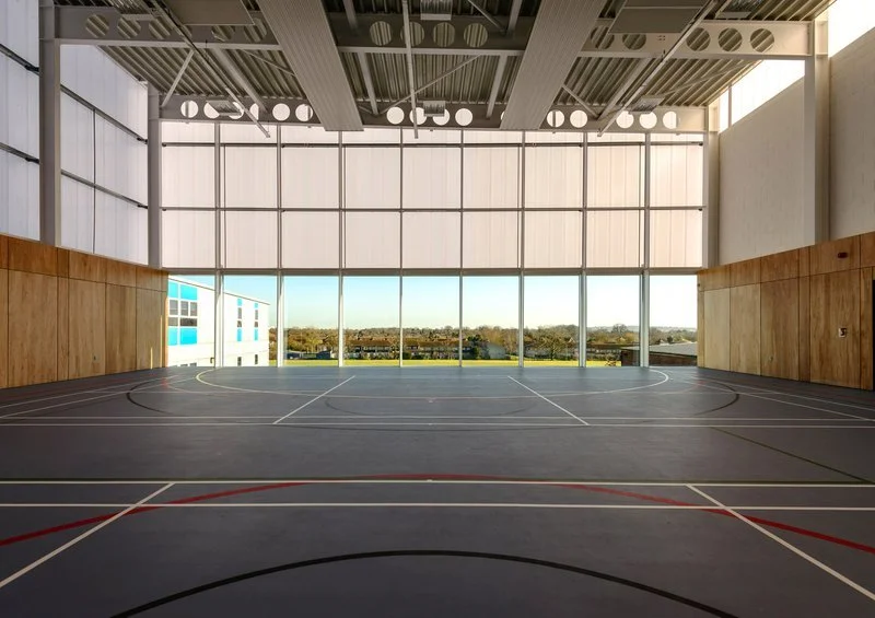 Indoor sports court with large glass windows and a view of trees outside.