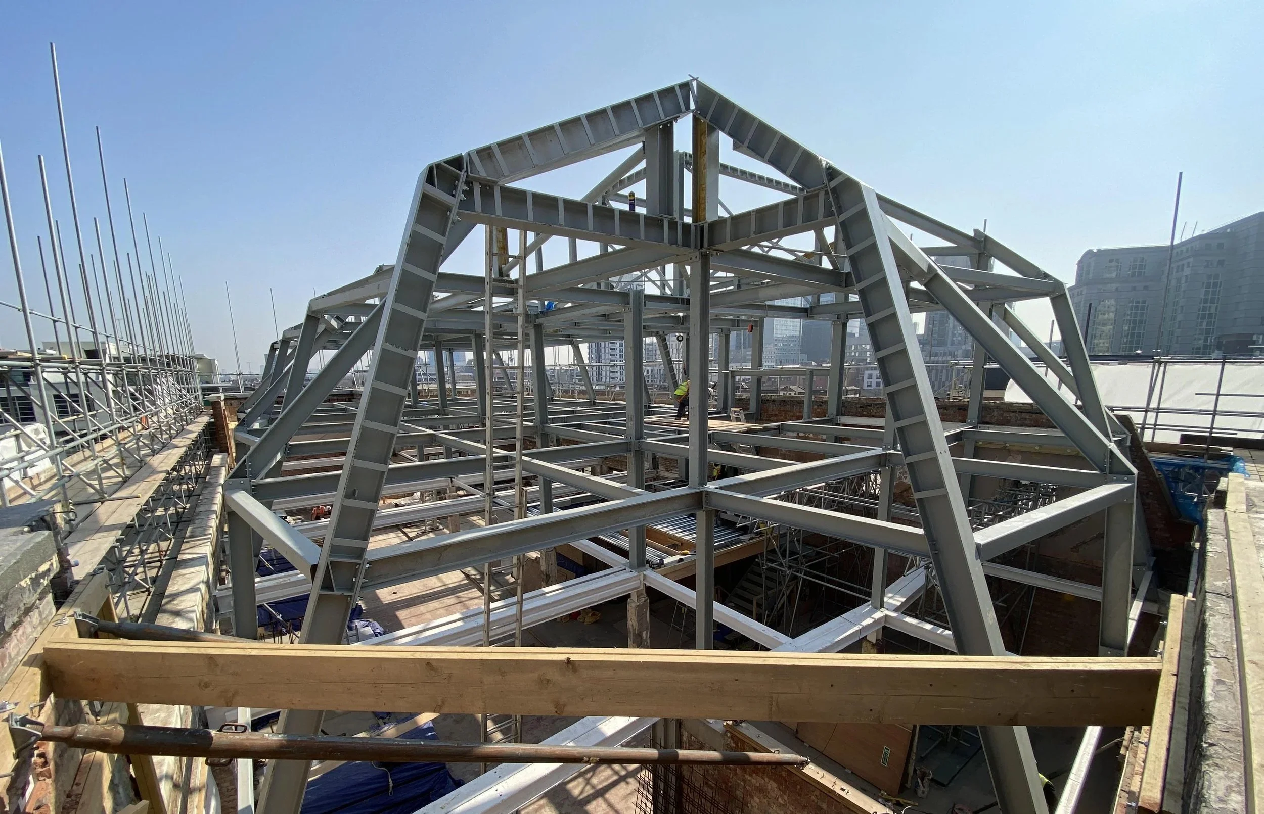 An on-site wide photograph of the massive, unclad steel frame erected on top of the building.
