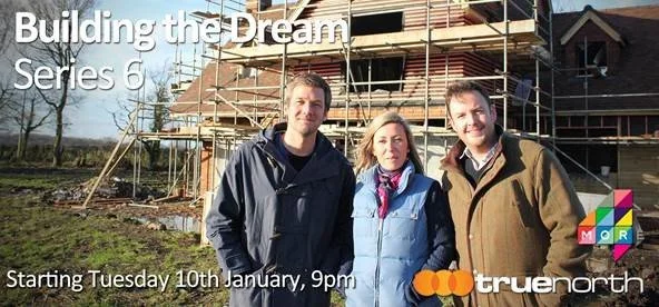 Three people standing in front of a construction site with a partially built house and scaffolding, promoting a TV series about building homes.