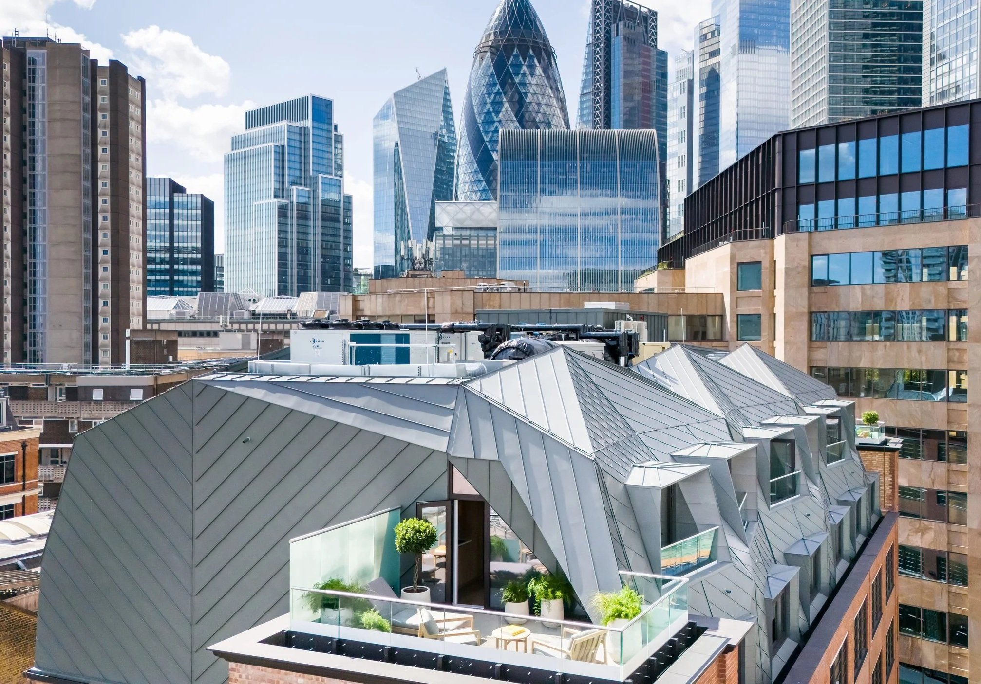 A cityscape with modern skyscrapers made of glass, an older office building, and a rooftop terrace with plants and outdoor furniture.