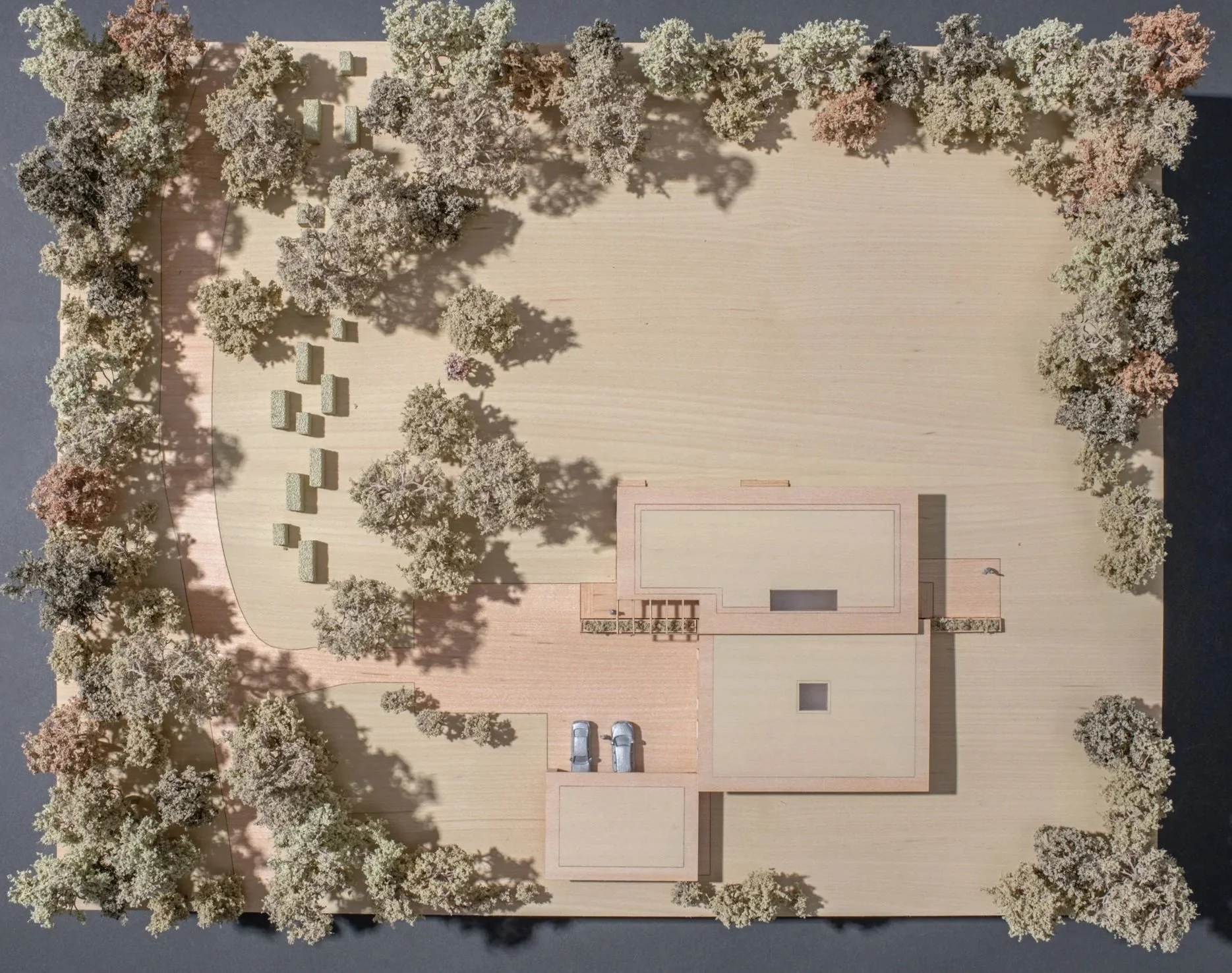 A detailed architectural model of a building surrounded by trees, with parking spaces and some outdoor features visible.