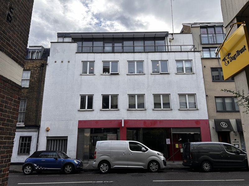 Street view of a white multi-story building with windows, with parked cars in front and a DogTrust sign on the side.