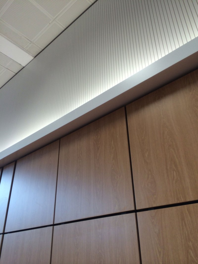 Close-up of a wooden wall with black lines dividing the panels, and a white textured ceiling above.