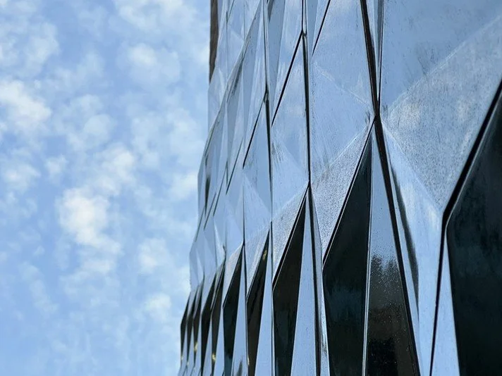 A low-angle close-up photograph looking up the facade of the Wilde Hotel, showcasing the glossy, green three-dimensional faceted tiles designed by NBA.