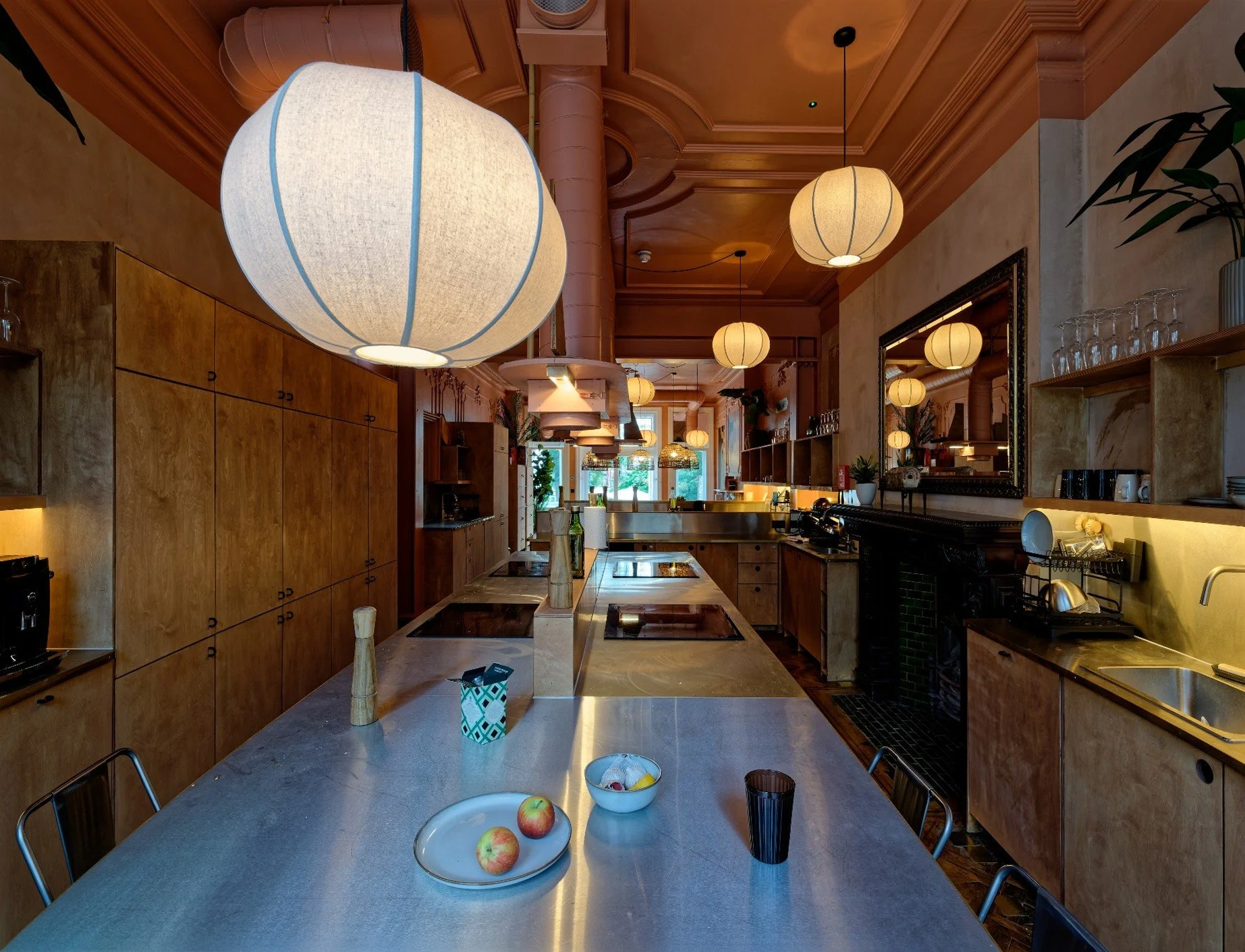 The image showcases the premium shared amenities within a Cohabs co-living building. open-plan communal kitchen and dining room defined by high ceilings with existing cornice details and warm salmon-pink paint.