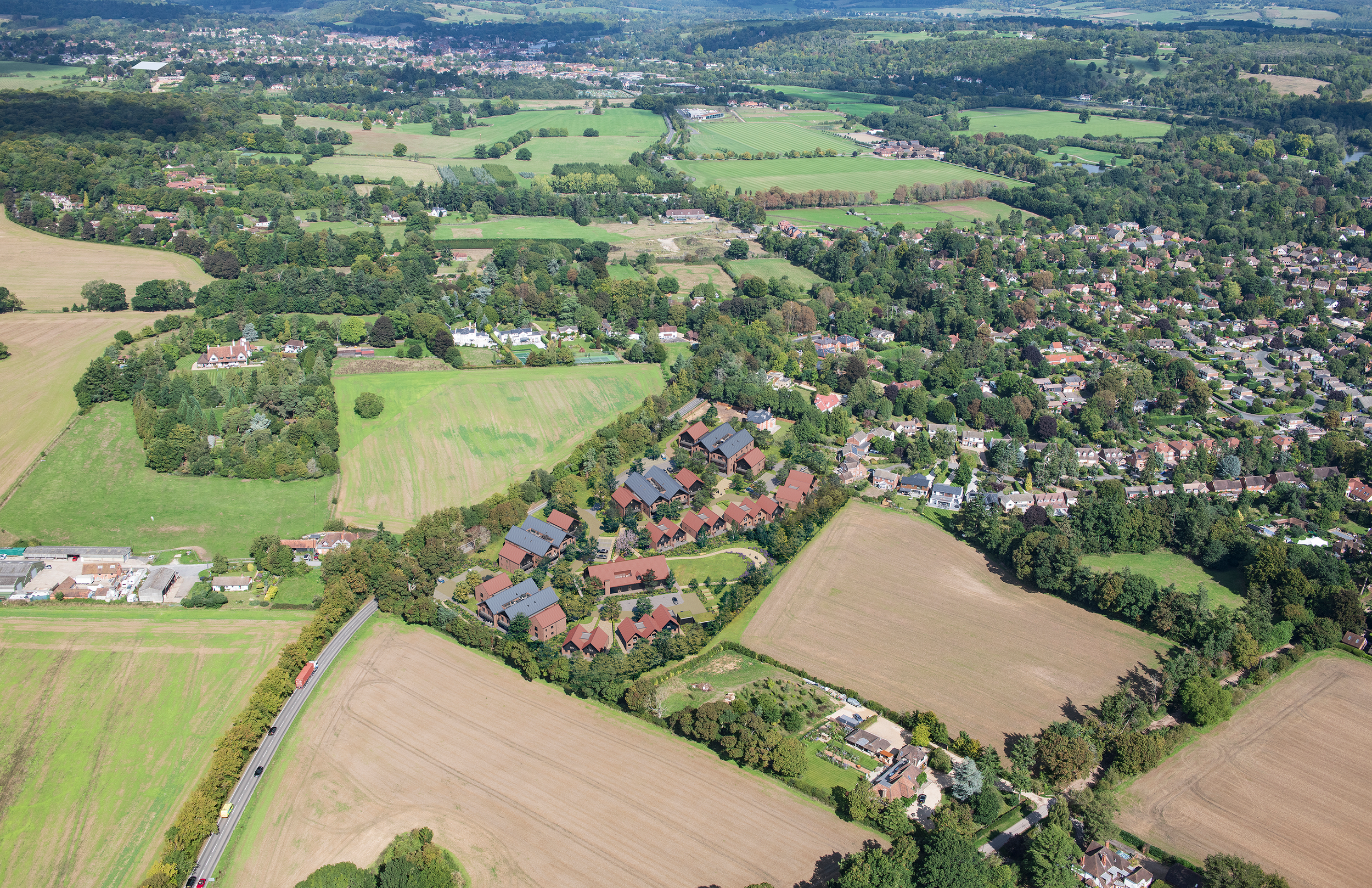 Aerial drone photograph of Shiplake Meadows residential masterplan scheme, showcasing cluster housing with pitched clay tile and grey metal roofs integrated into the south of Henley-on-Thames, Oxfordshire, England. countryside landscape.