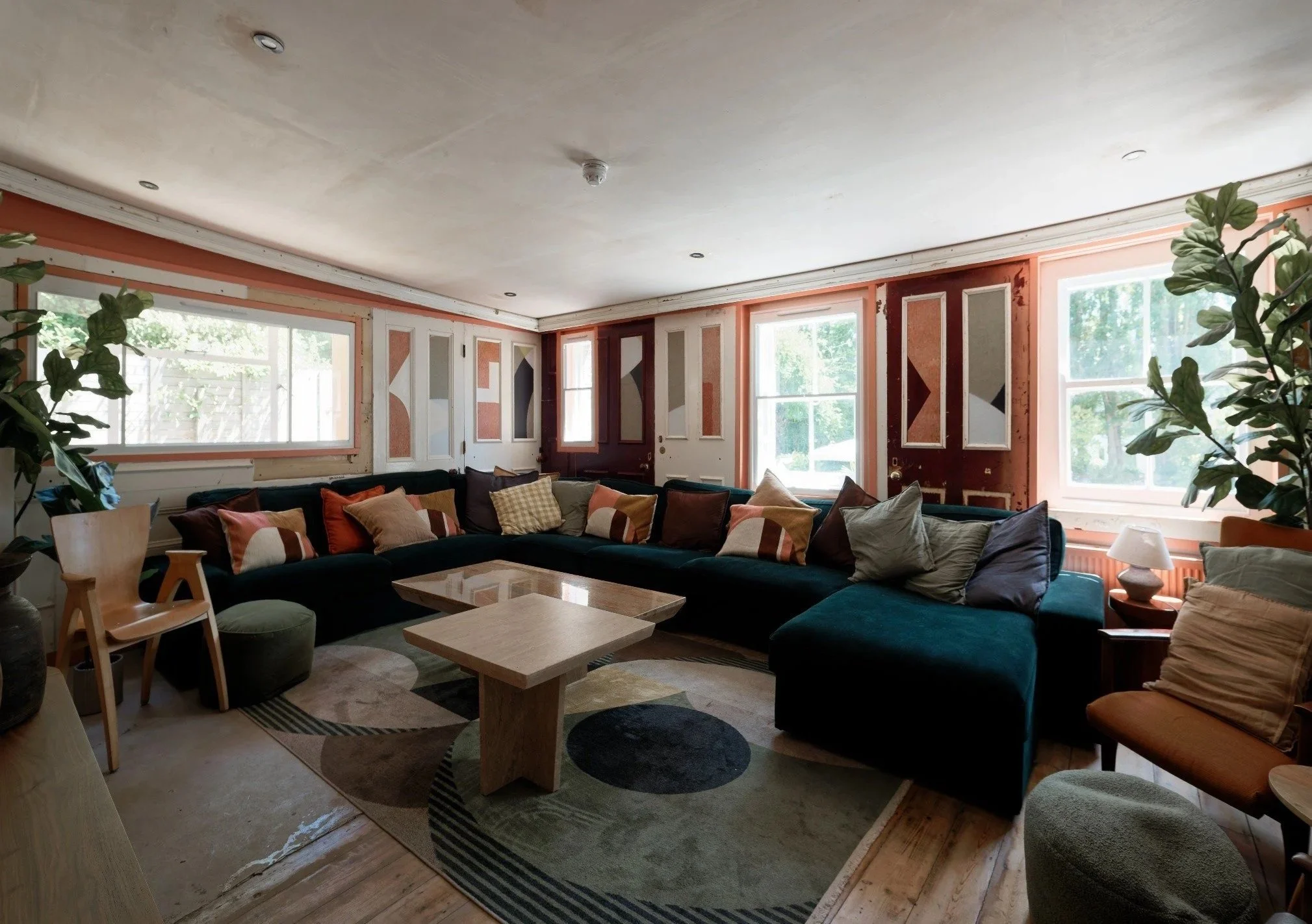 Living room with large sectional sofa, multiple pillows, coffee tables, and windows letting in natural light, some plants, and ceiling recessed lighting.
