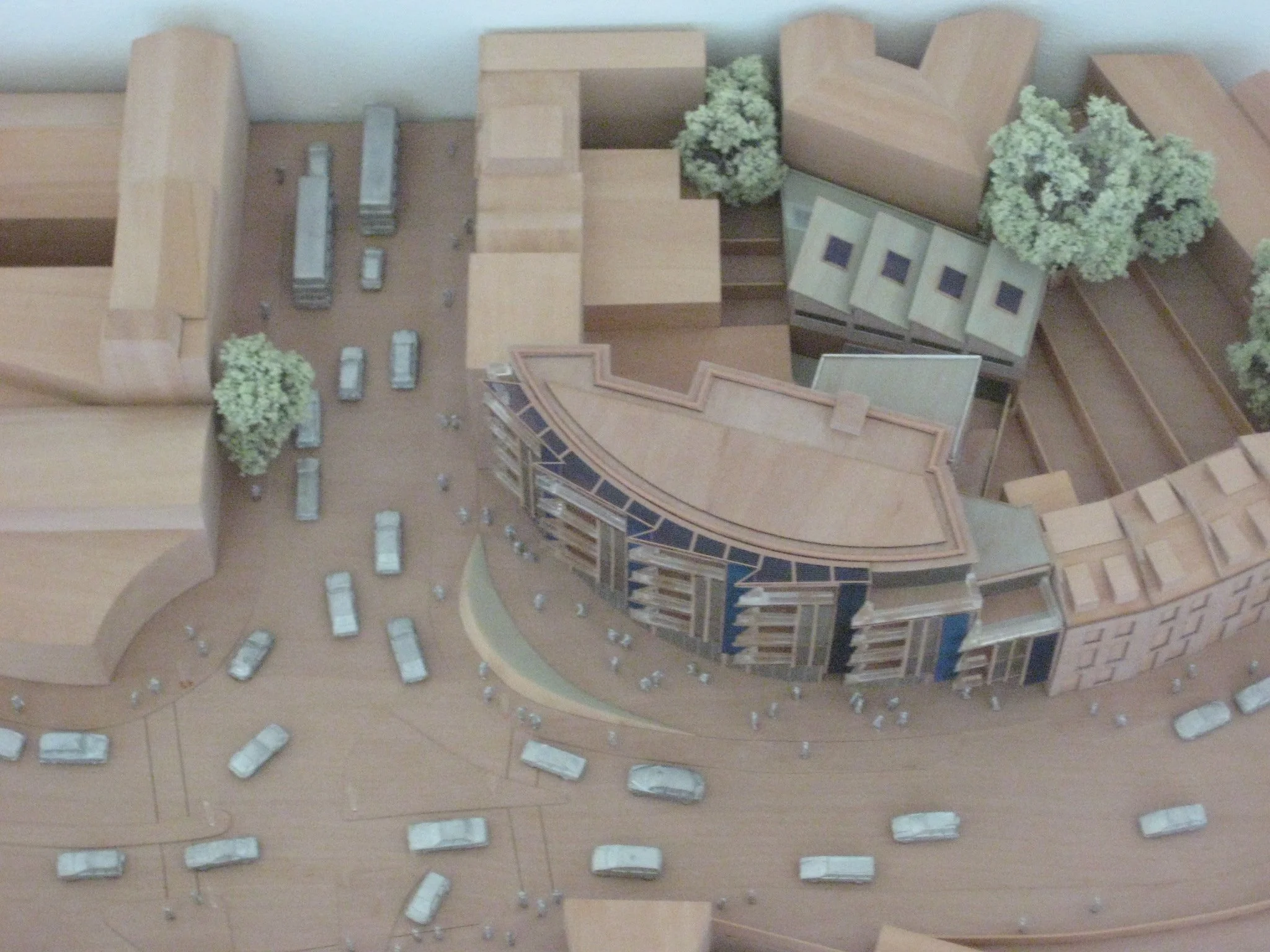 High-angle view of a physical wooden massing model illustrating the urban site context and curved footprint of a 5-storey development design on a prominent corner plot.