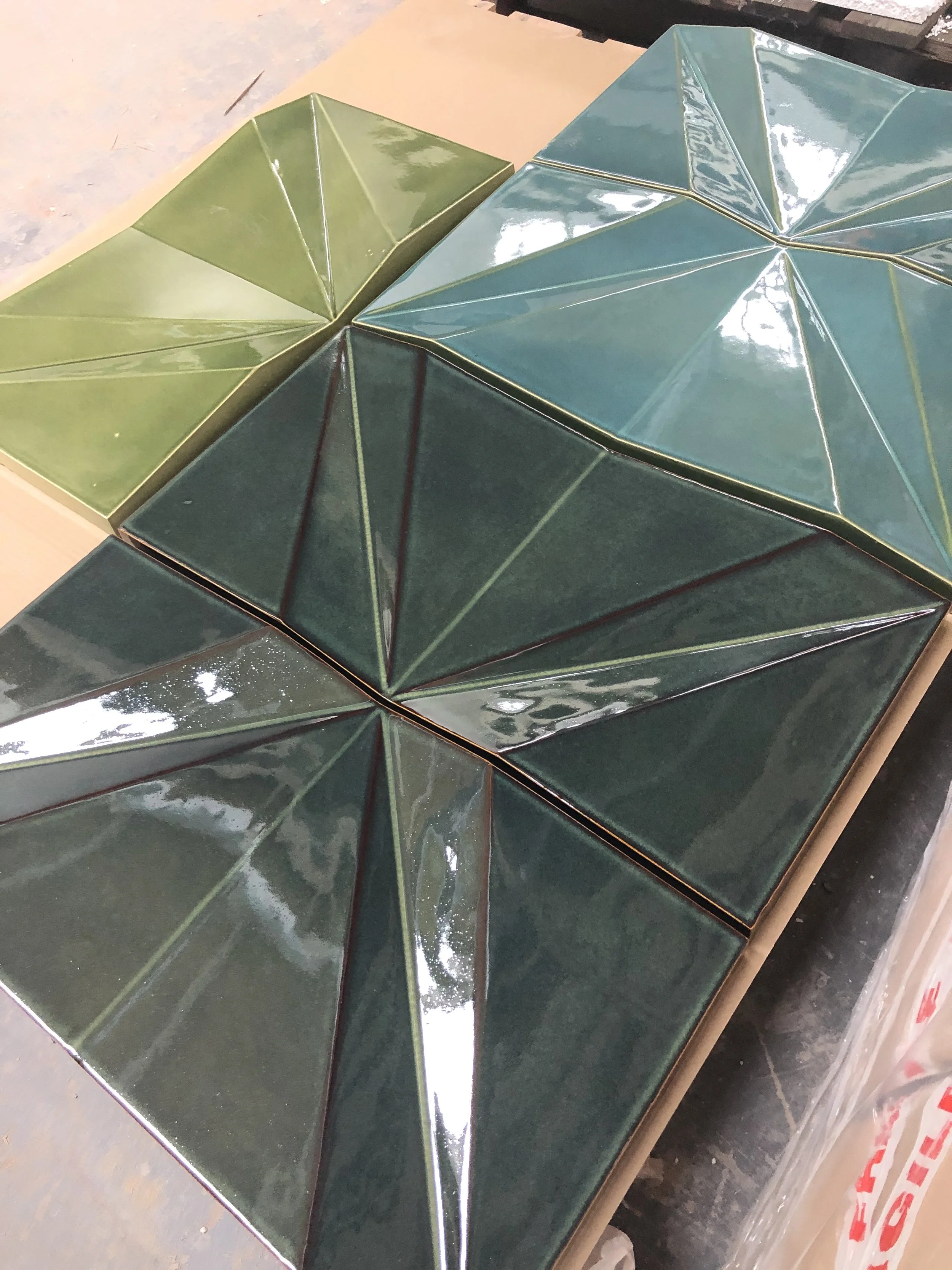 Close-up of geometric ceramic tiles with triangular facets in different shades of green.