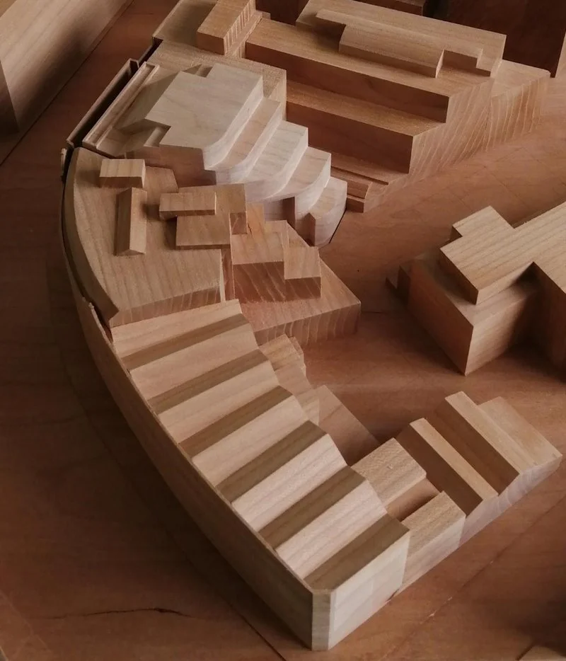 A wooden architectural model of a multi-level structure with stairs, platforms, and sections, likely representing a building or landscape design.