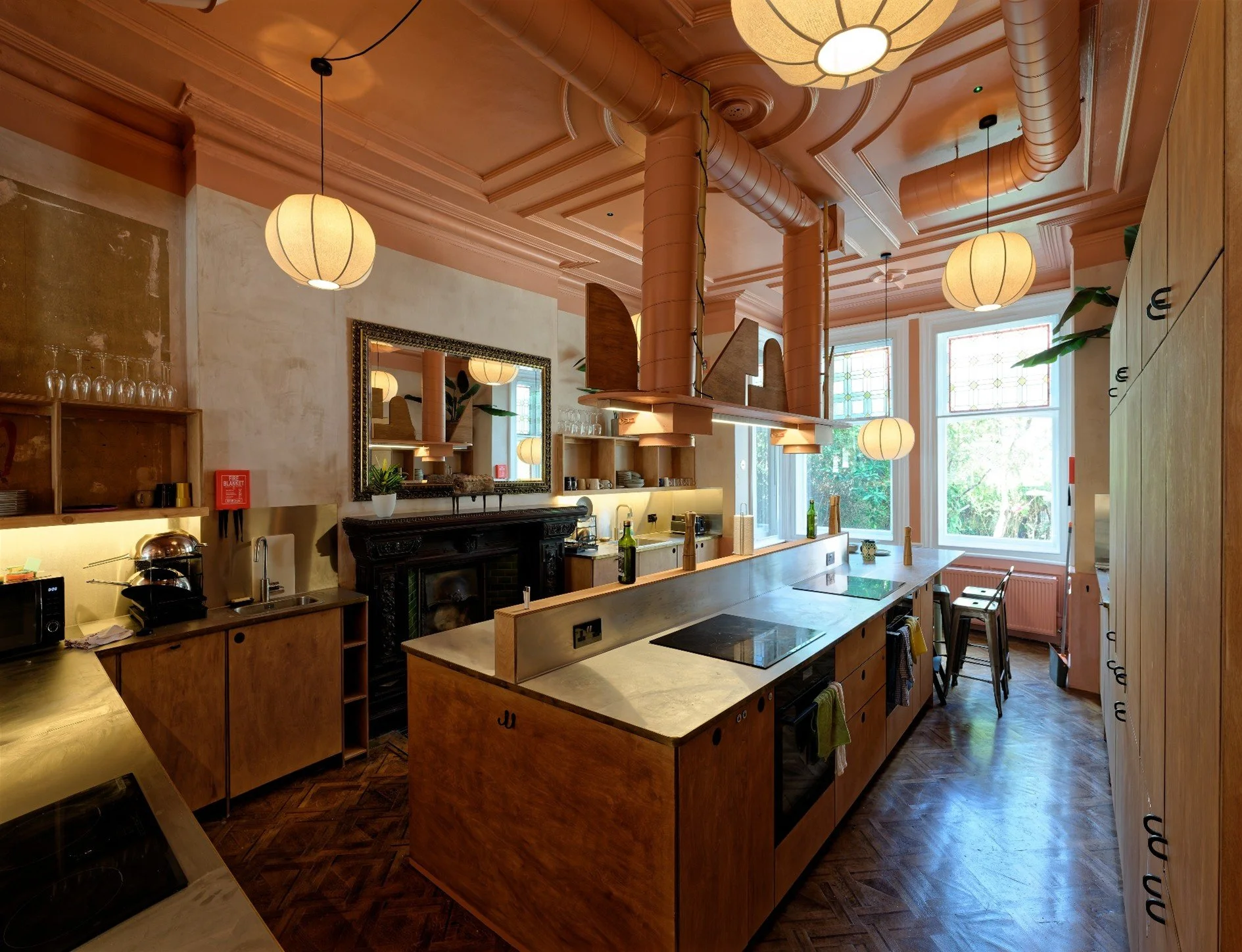The image showcases the premium shared amenities within a Cohabs co-living building. open-plan communal kitchen and dining room defined by high ceilings with existing cornice details and warm salmon-pink paint.