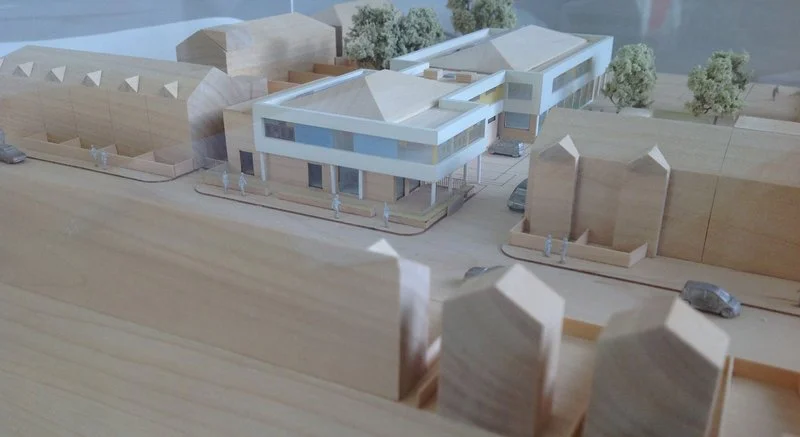 Architectural model of a modern building with trees, cars, and surrounding structures.