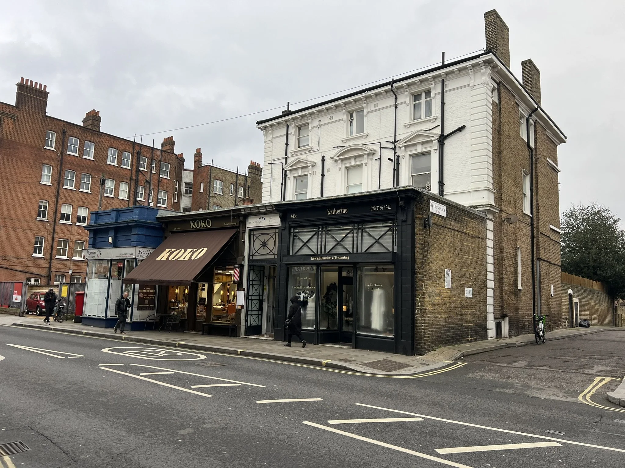 A street-level photograph looking along Fulham Road, showing the front facade of a historic building with ground-floor commercial shops.