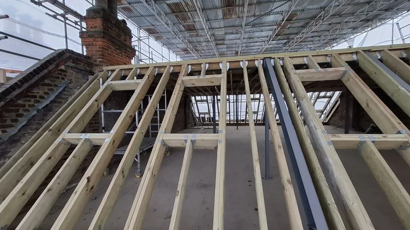 Wooden framing structure under construction in a building with scaffolding and protective roof.
