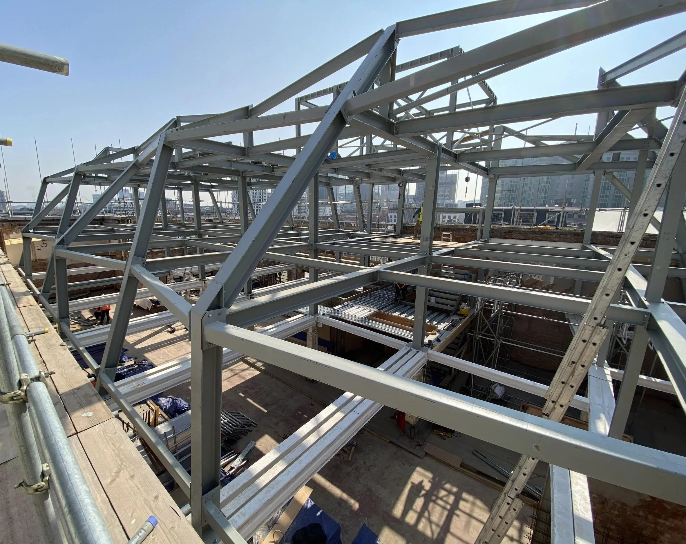 An on-site wide photograph of the massive, unclad steel frame erected on top of the building.