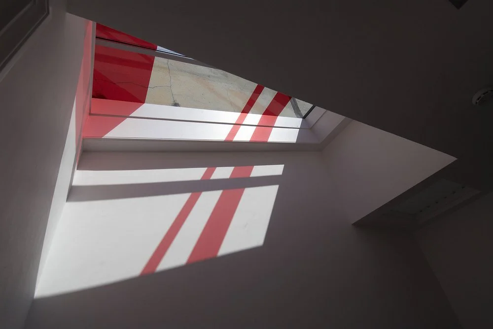 Interior photo of the final built rooflight designed by NBA, showing sunlight casting distinct red geometric shadows onto the white walls inspired by the Austrian flag.