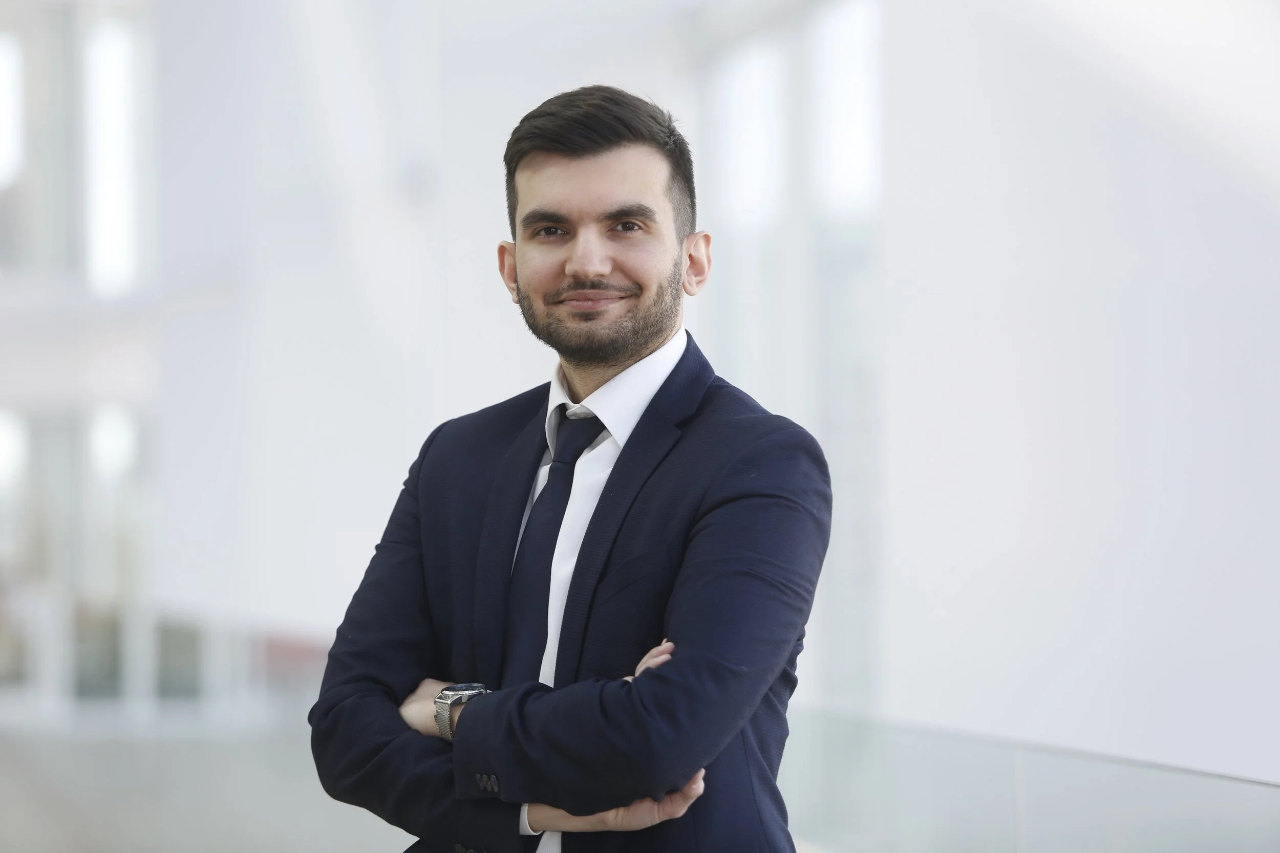 Zakelijke man in pak met armen gekruist, glimlach, neutrale achtergrond, moderne kantooromgeving.