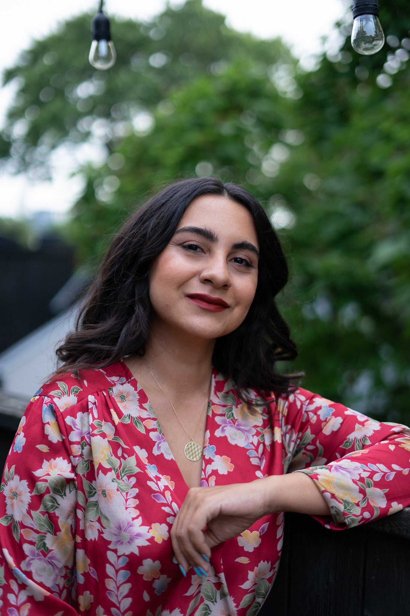 A young woman is outdoors with blurred green trees in the background.