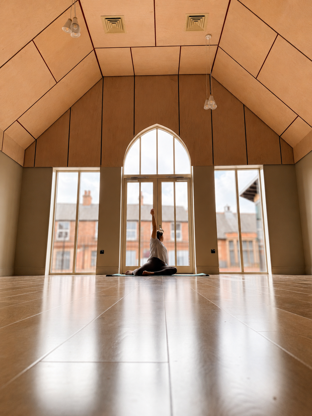 A person practicing yoga in a bright, spacious room with high, wooden-paneled ceiling and large windows.
