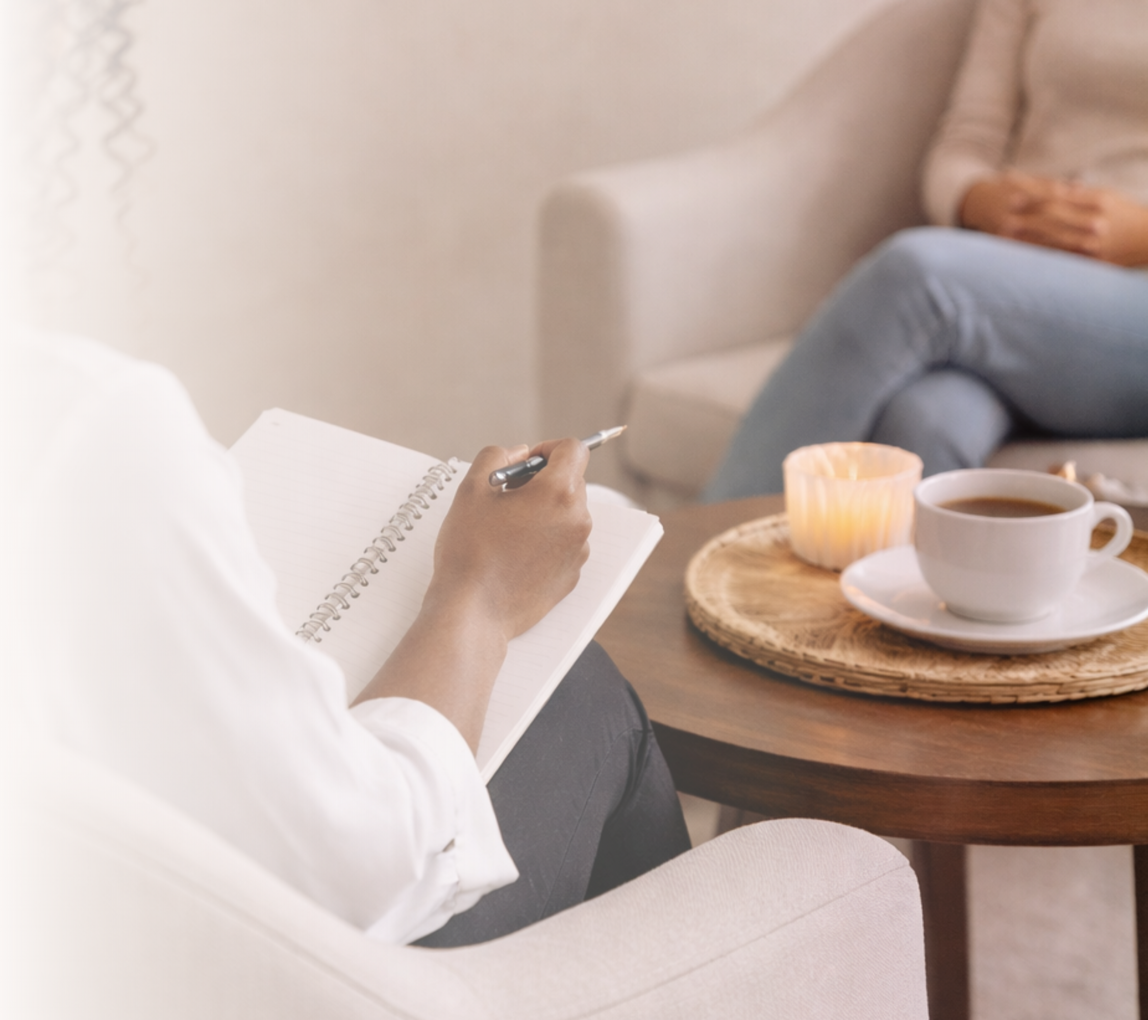 Person sitting at a table with coffee, cup, and baked goods, writing in a notebook, in a cozy indoor setting.