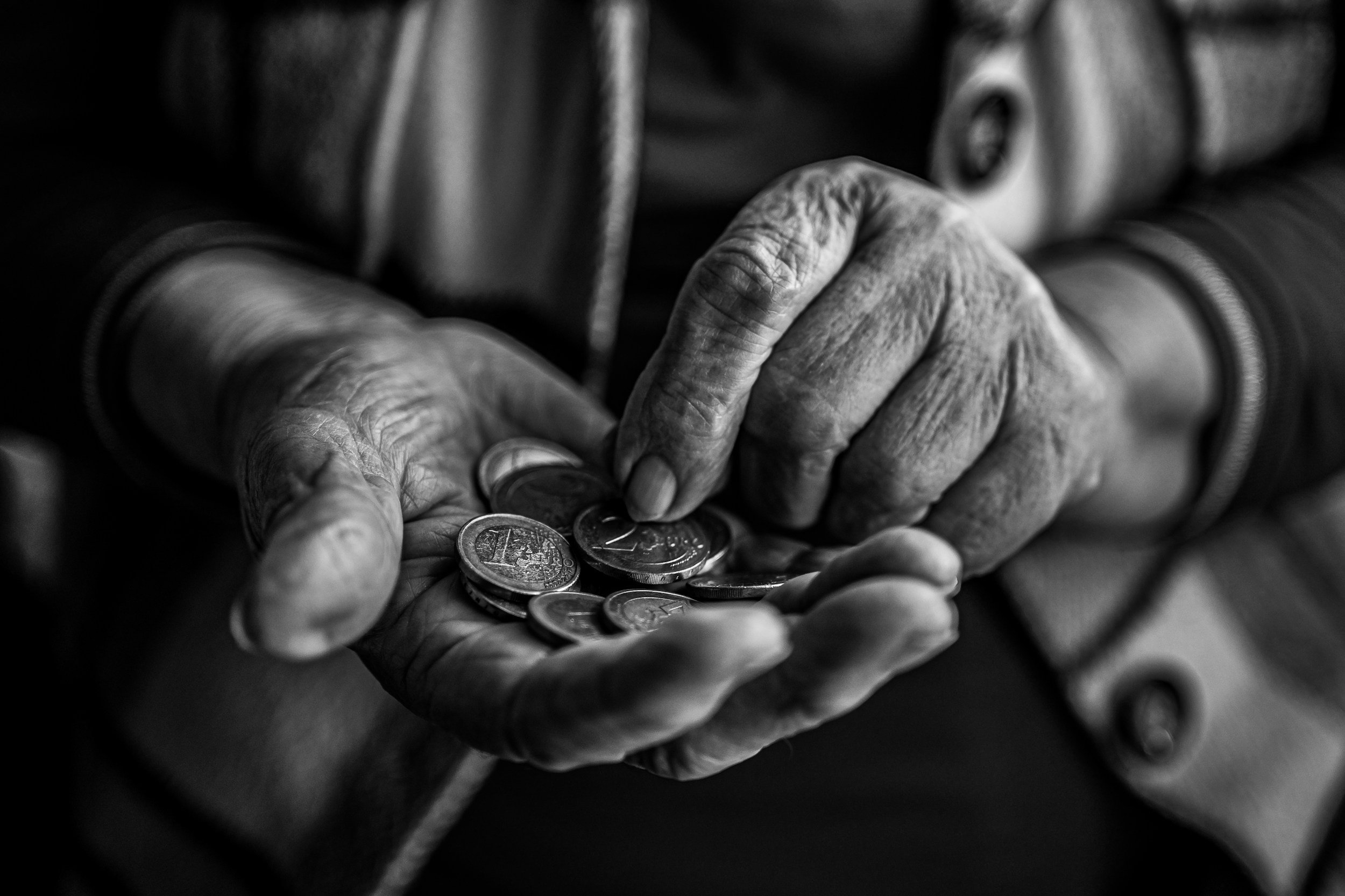 Close-up black and white photo of elderly person's wrinkled hands counting coins.