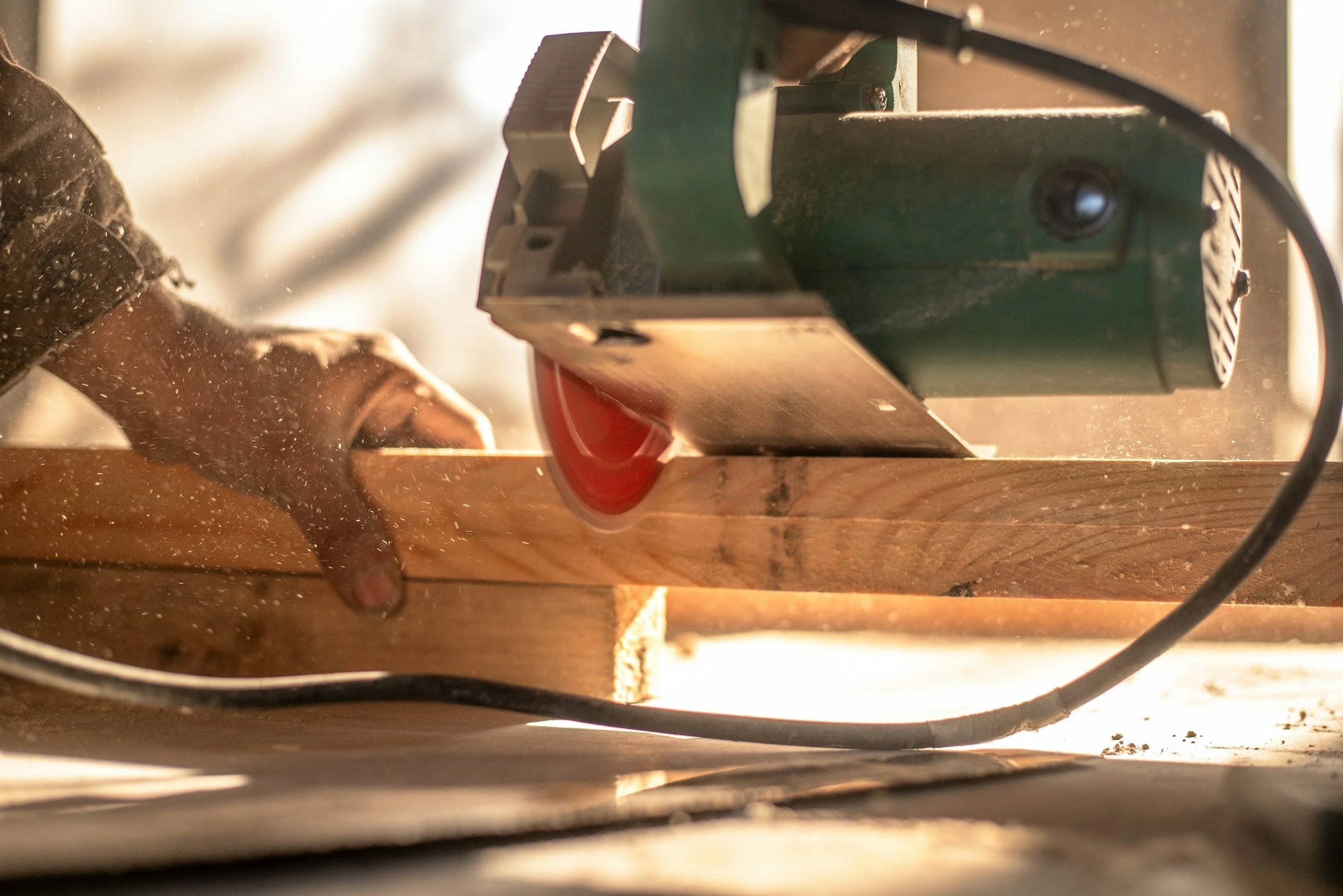 A person using a circular saw to cut a piece of wood, with sawdust flying in the air.