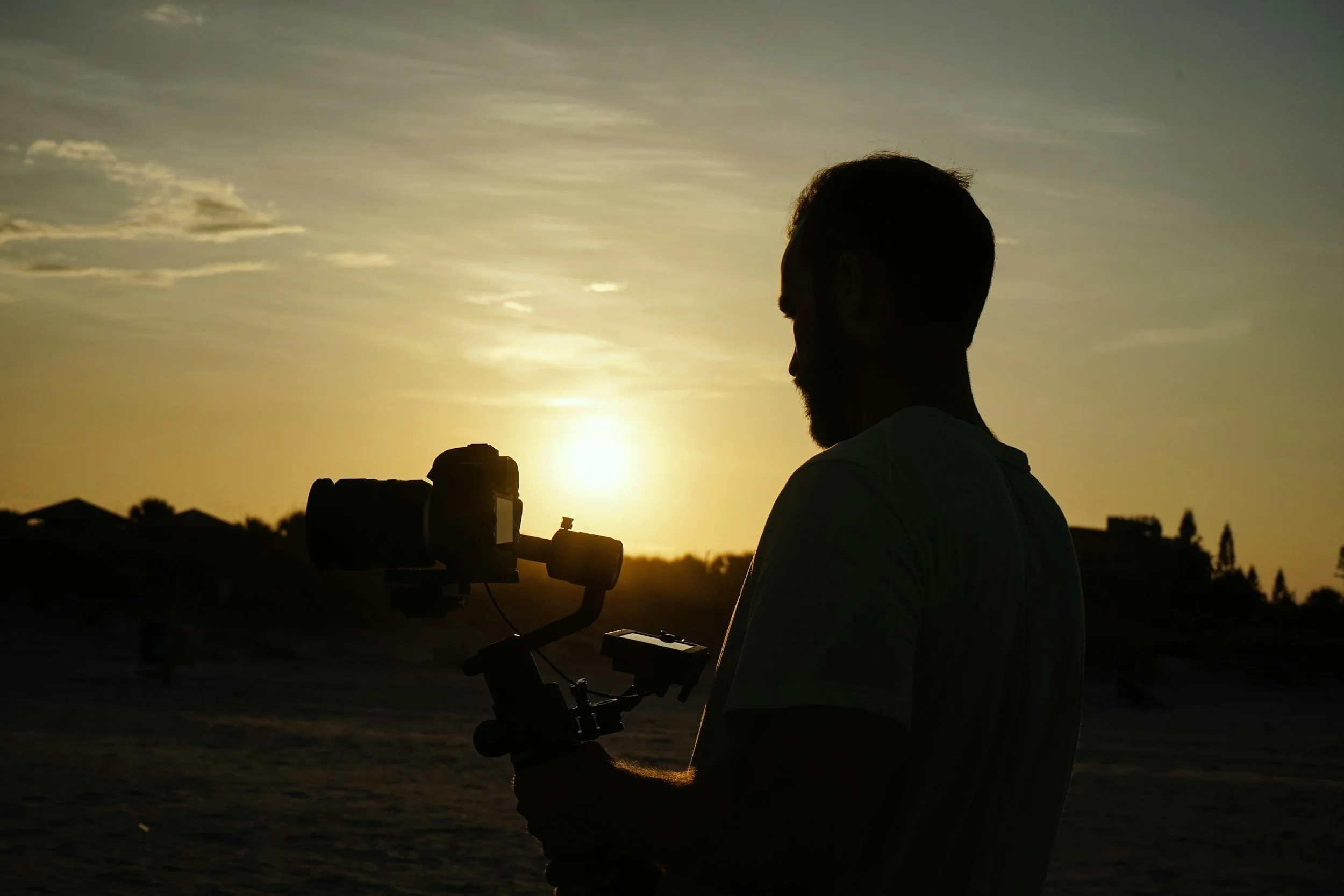 Silhouette of a person setting up a camera outdoors during sunset or sunrise.