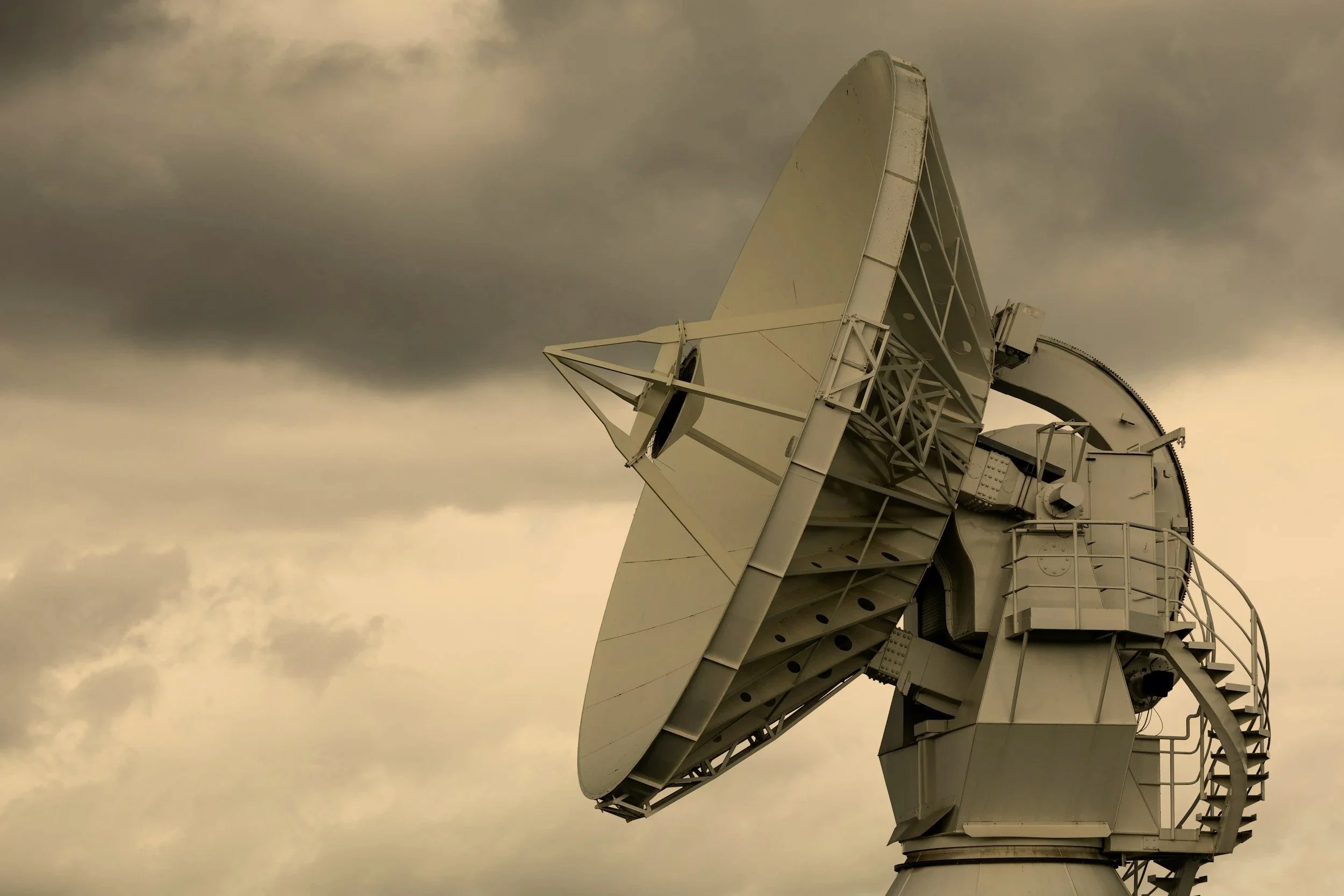 A large satellite dish antenna pointing upward against a cloudy sky.