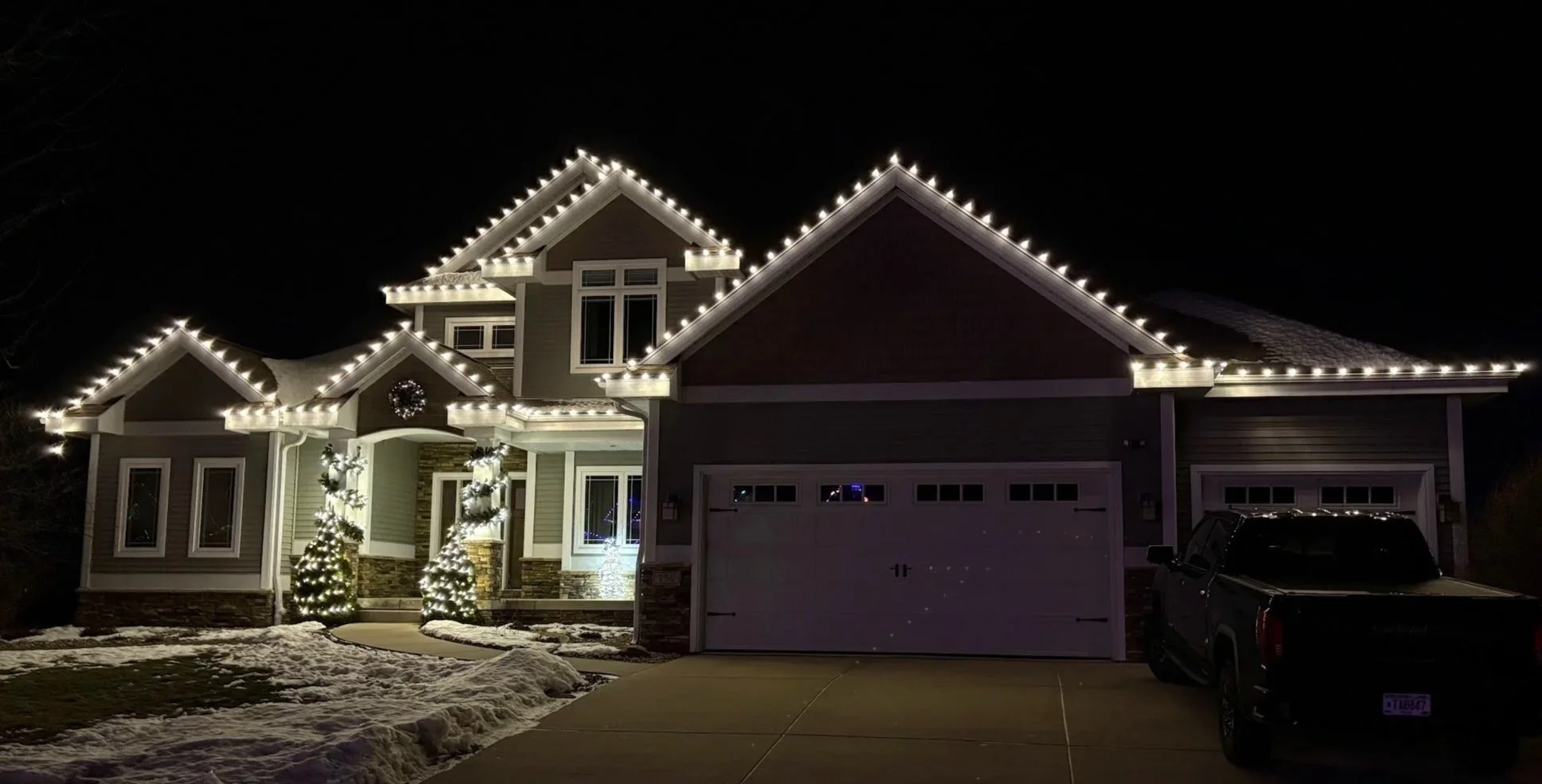 A large house decorated with Christmas lights, wreaths, and Christmas trees, with a well-manicured front yard.
