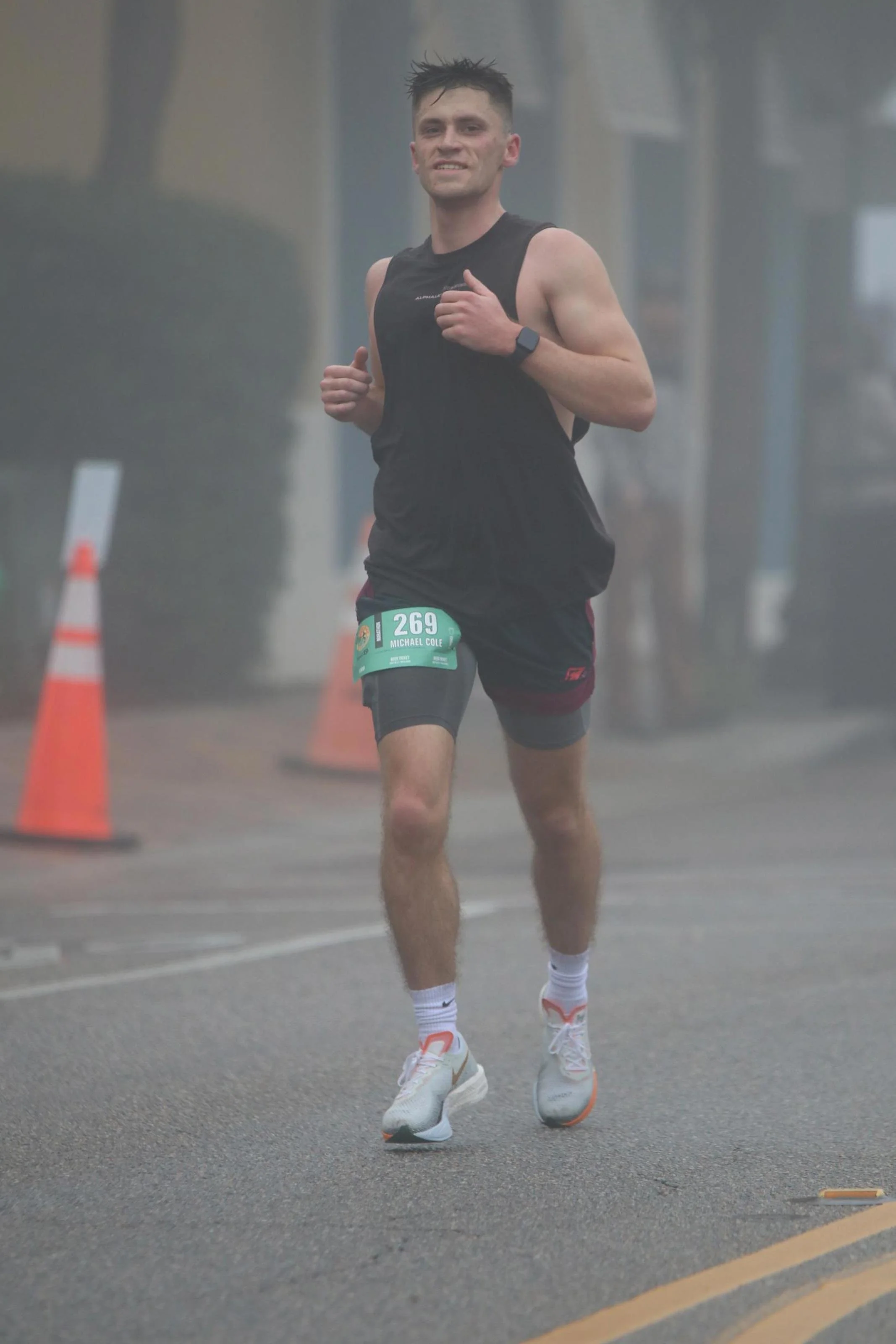 Man running in a street marathon, wearing black athletic clothing, a race bib with number 269, and white running shoes.