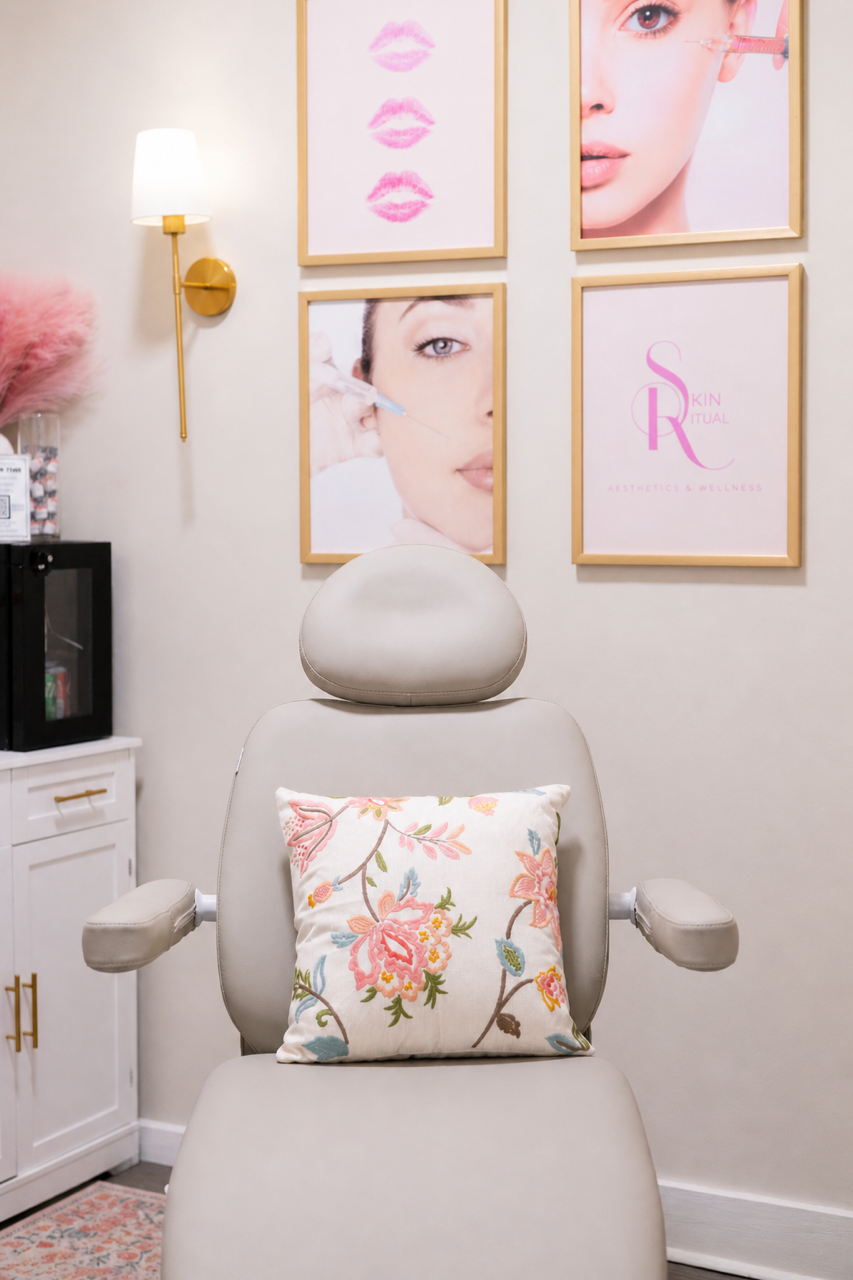 An empty treatment chair in a beauty clinic with floral pillow, framed beauty-related posters on the wall, a lamp, and a cabinet with skincare products. Skin Ritual Aesthetics & Wellness in Ridgeville, SC offers Botox, dermal fillers, microneedling,