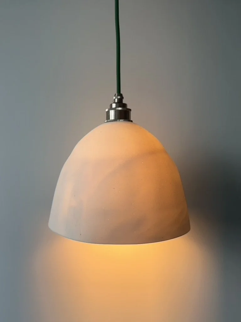 A hanging pendant light with a beige shade emitting warm light against a plain gray wall.