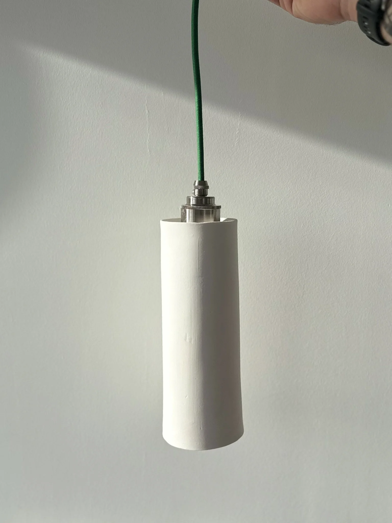 Close-up of a green wire connected to a metal fitting inside a white cylindrical object against a plain light gray background.