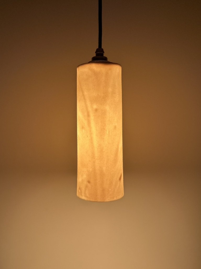 A hanging pendant light with a cylindrical beige shade, illuminating a room with a warm glow.