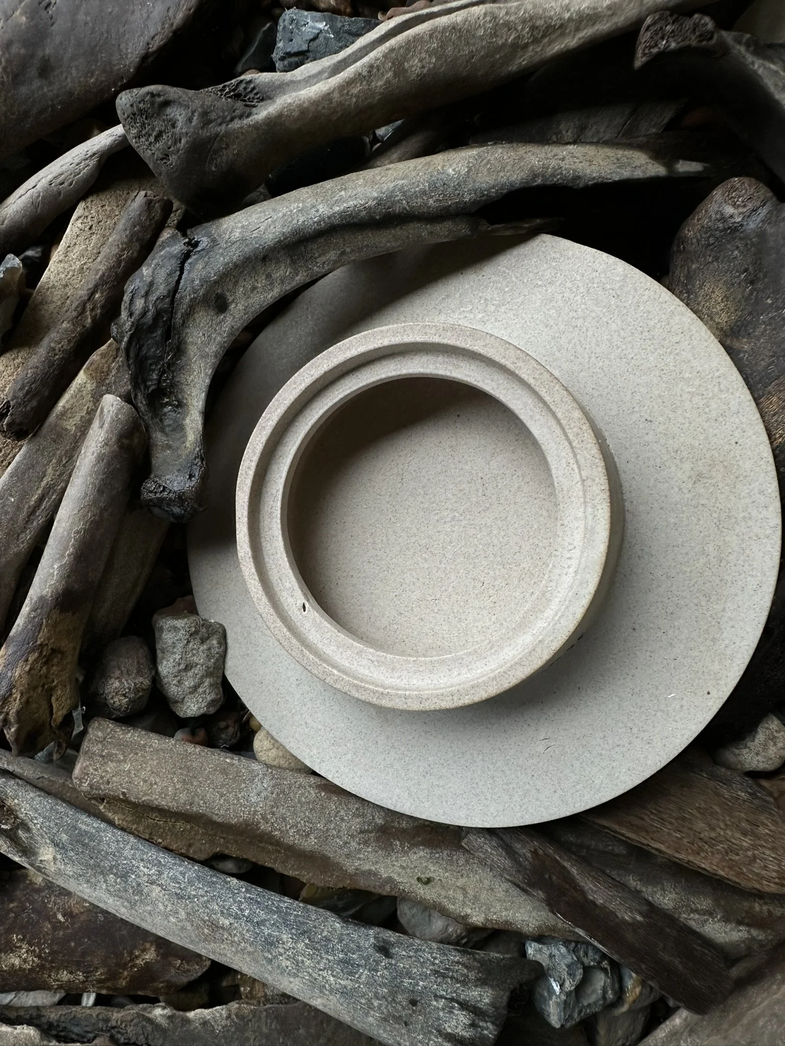 Close-up of a circular stone or concrete structure surrounded by driftwood and small rocks.