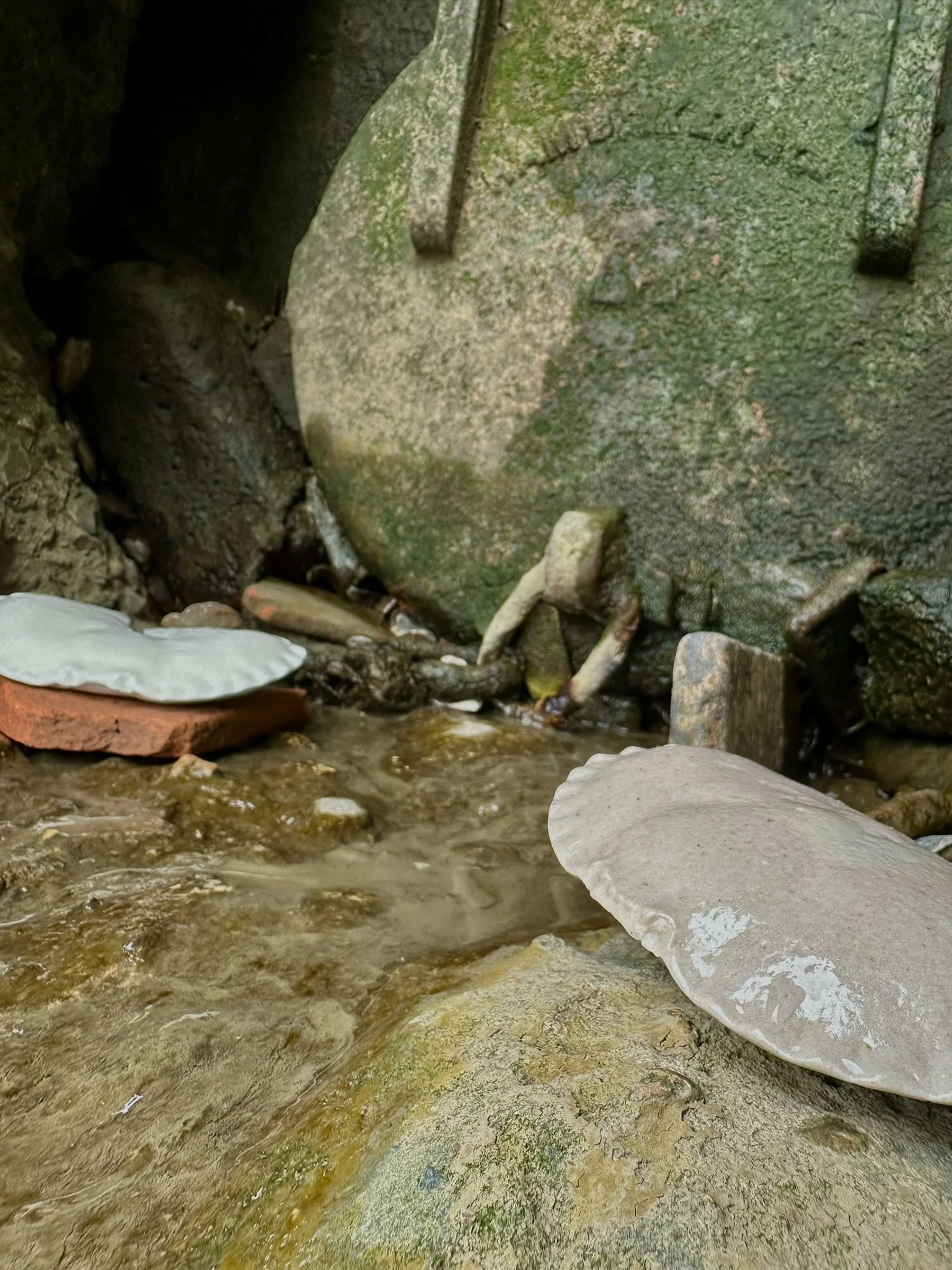 Close-up of a moss-covered stone wall with a small stream of water flowing over rocks in the foreground.