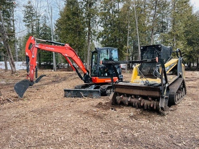 Construction site with two mini excavators in a wooded area.