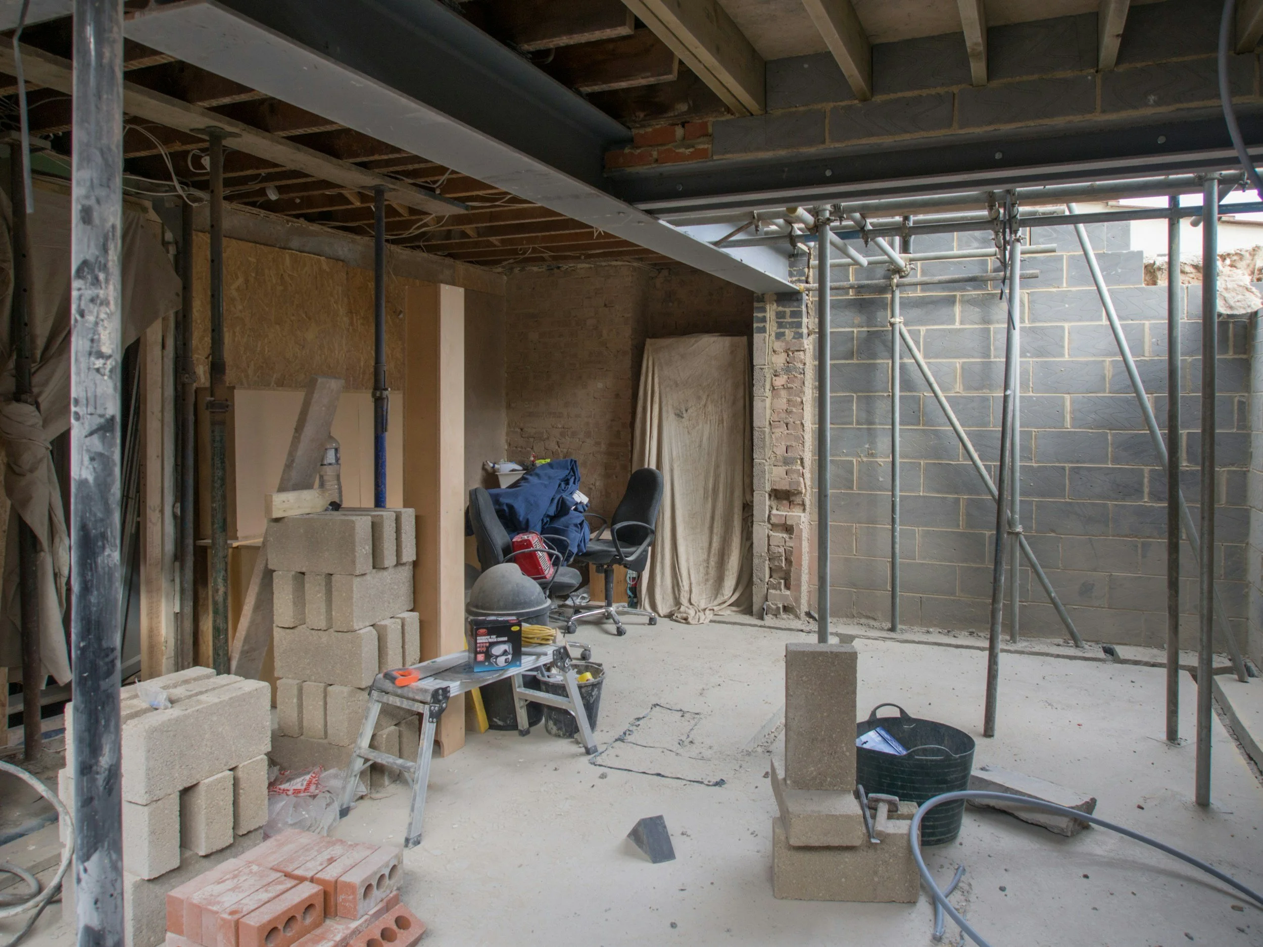 Interior view of a construction site with scaffolding, bricks, construction tools, and partially finished walls.