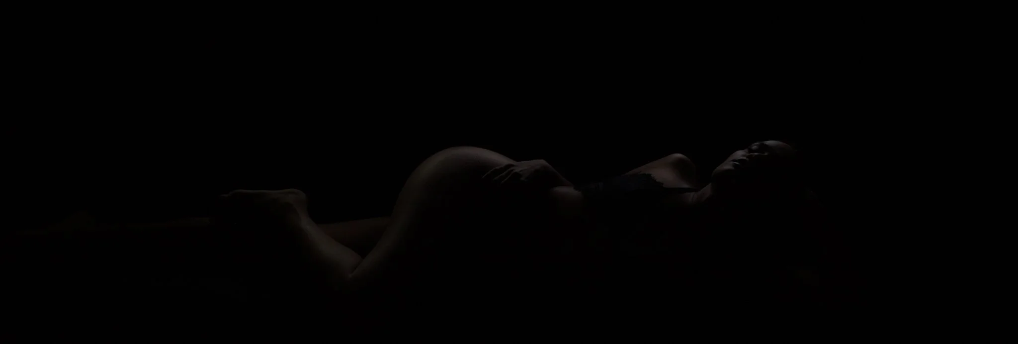 A person lying on their back in a dark room, with barely visible features illuminated.