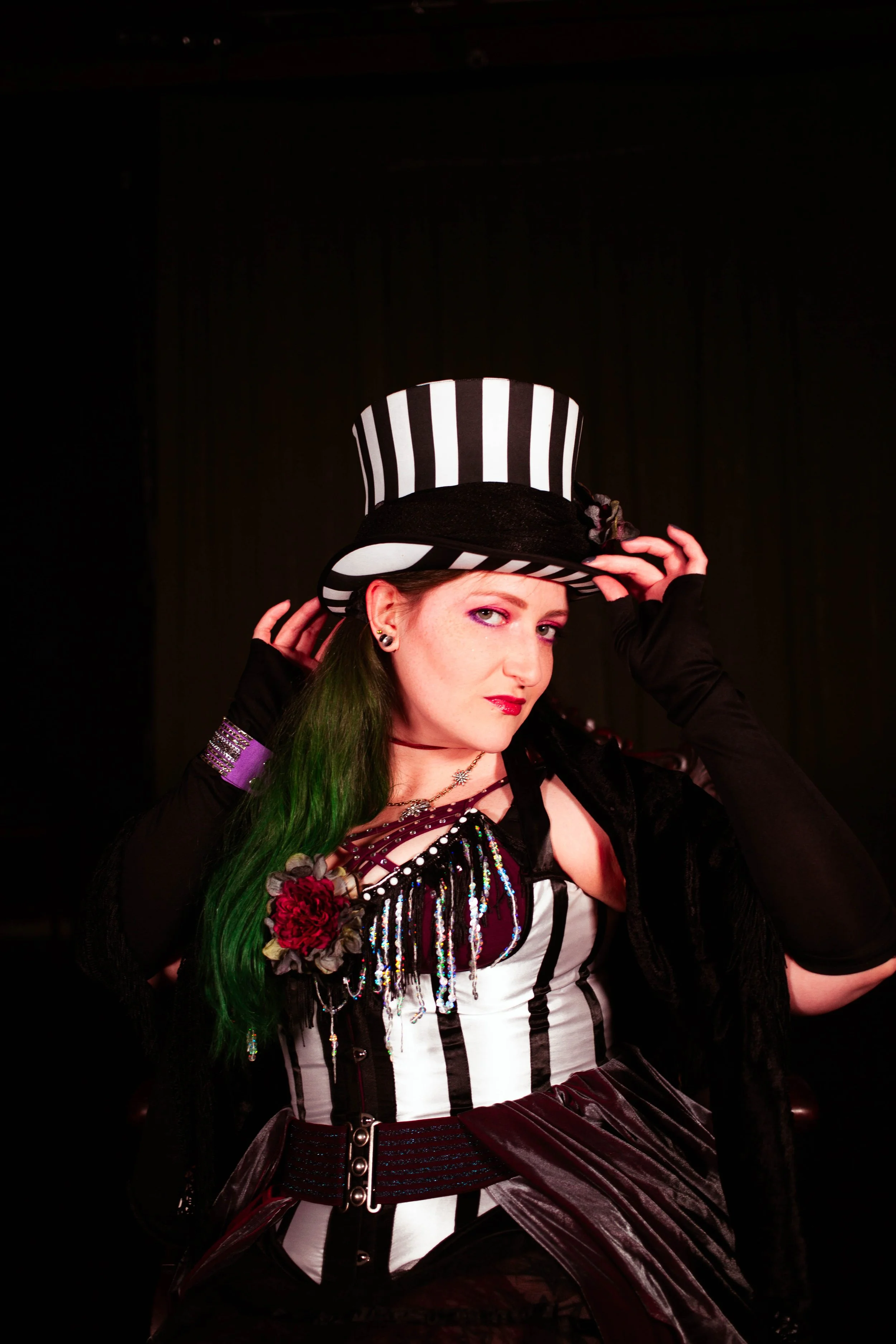 A woman dressed in a black and white striped costume with a large top hat, standing against a dark background.
