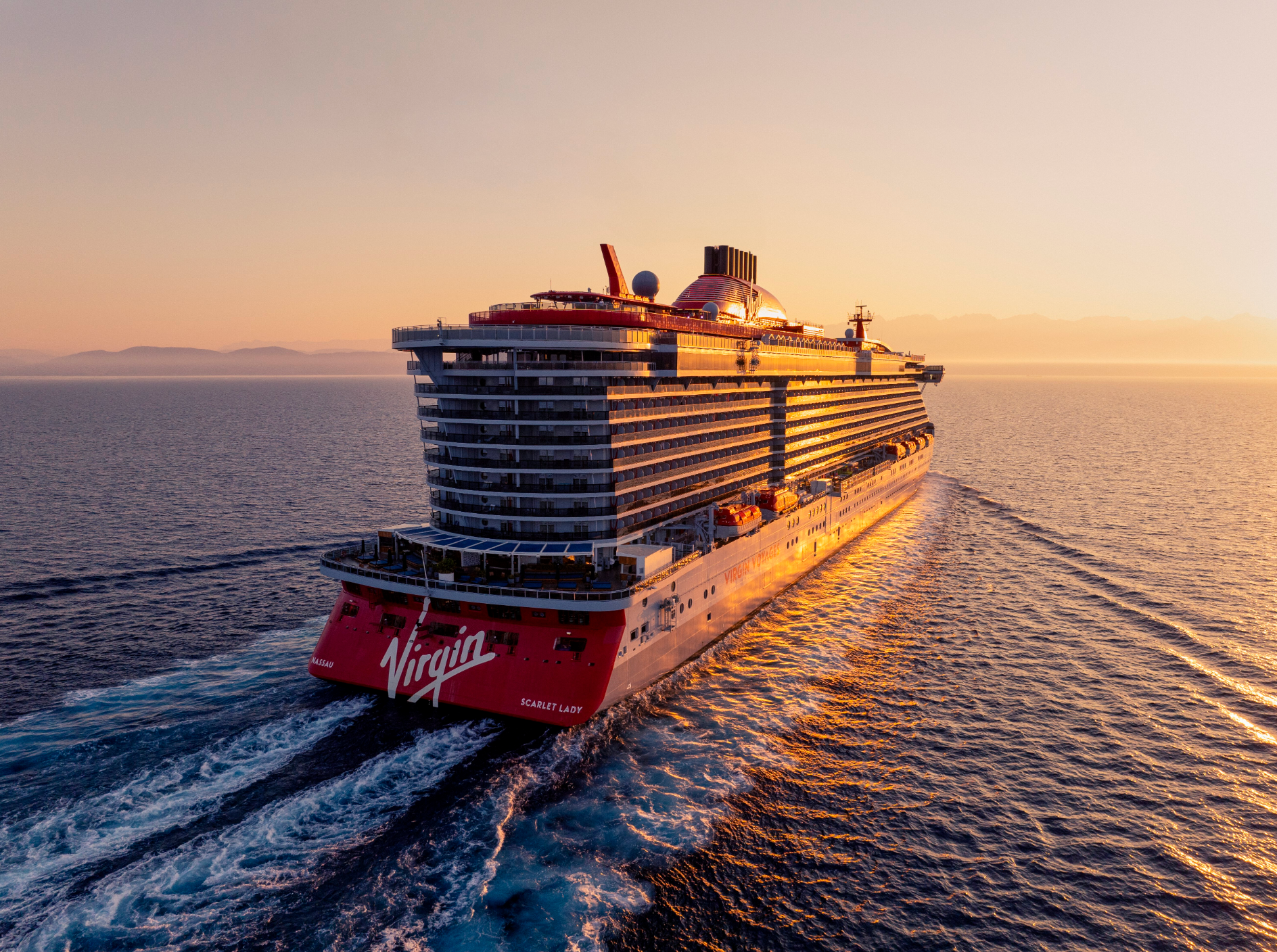 A large cruise ship named Virgin is sailing on the ocean during sunset, leaving a wake behind it.